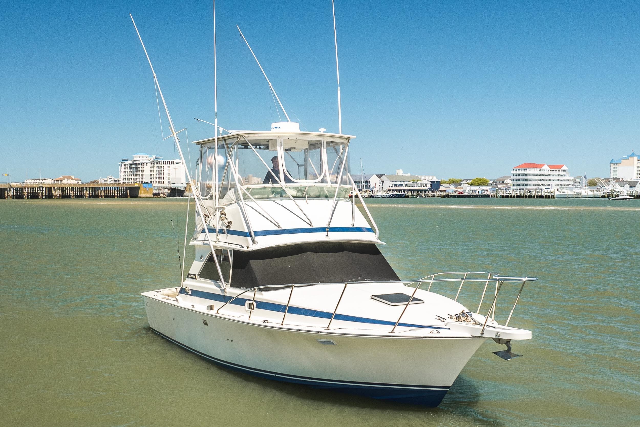 1986 Bertram 35 Flybridge Sportfish boat on calm water near a coastal cityscape.