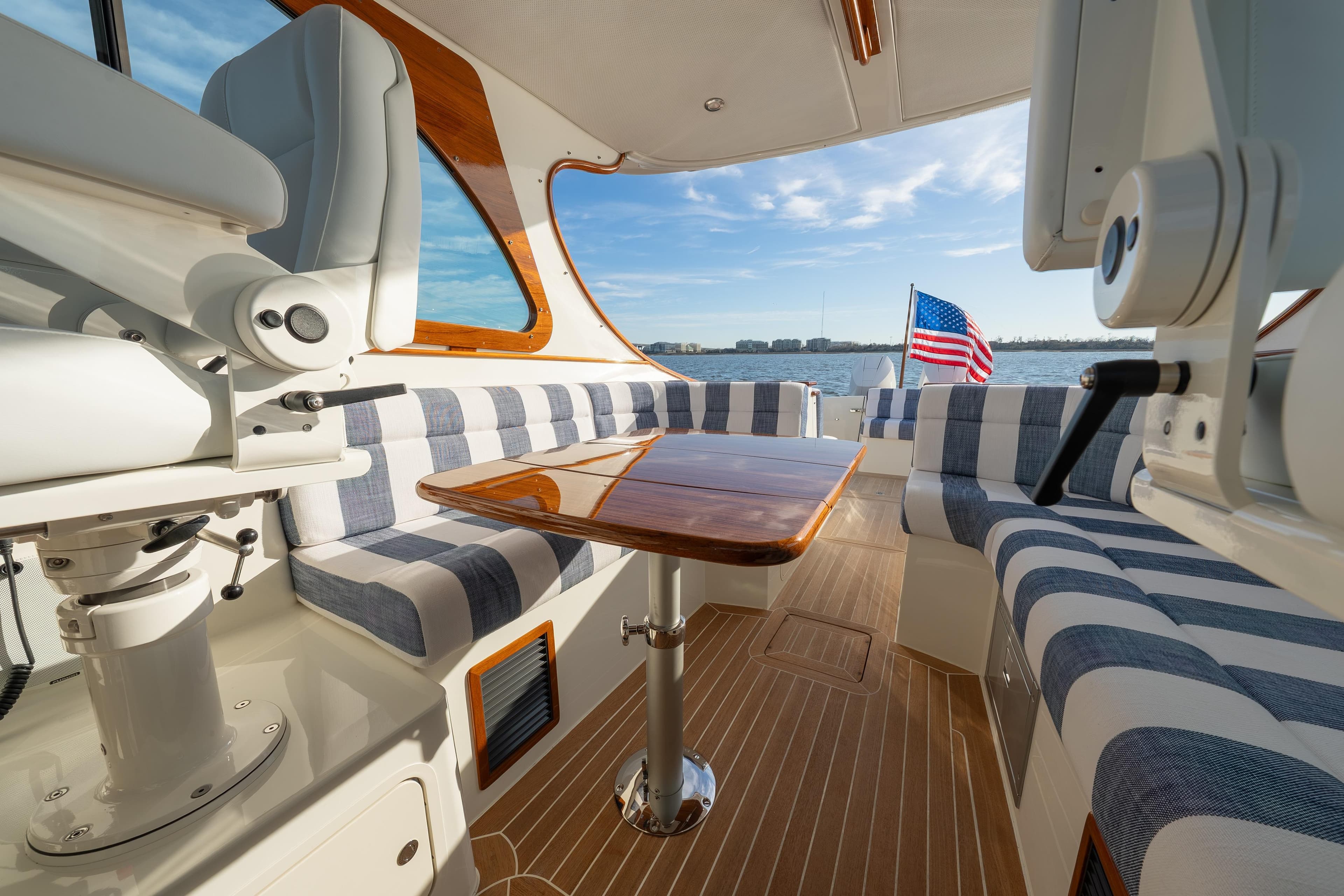 Interior of 2024 Hinckley 35 yacht with striped seating and wooden table, overlooking water.