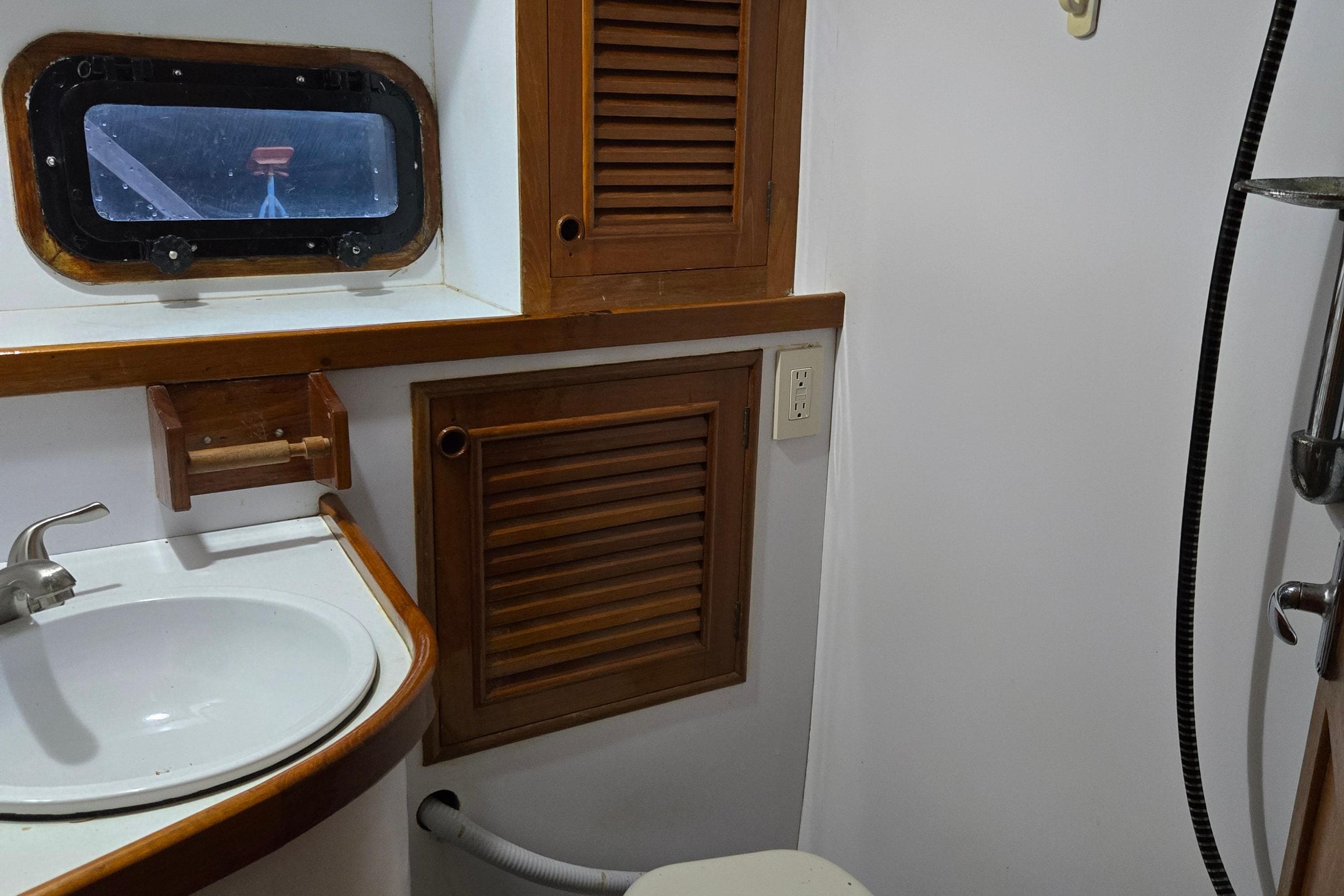 1981 Cheoy Lee 43 Pilot House bathroom with sink, wooden cabinets, and porthole window.
