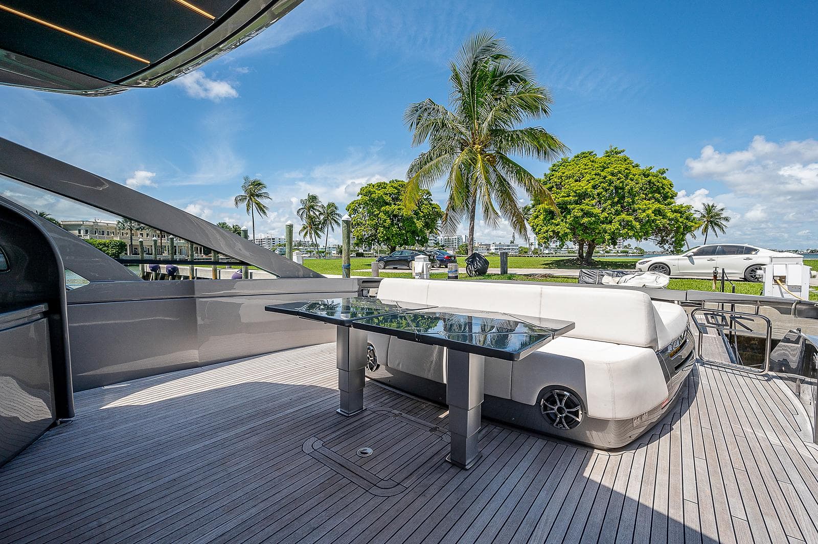 Luxurious 2015 Pershing 70 yacht deck with seating, glass table, and scenic palm tree view.