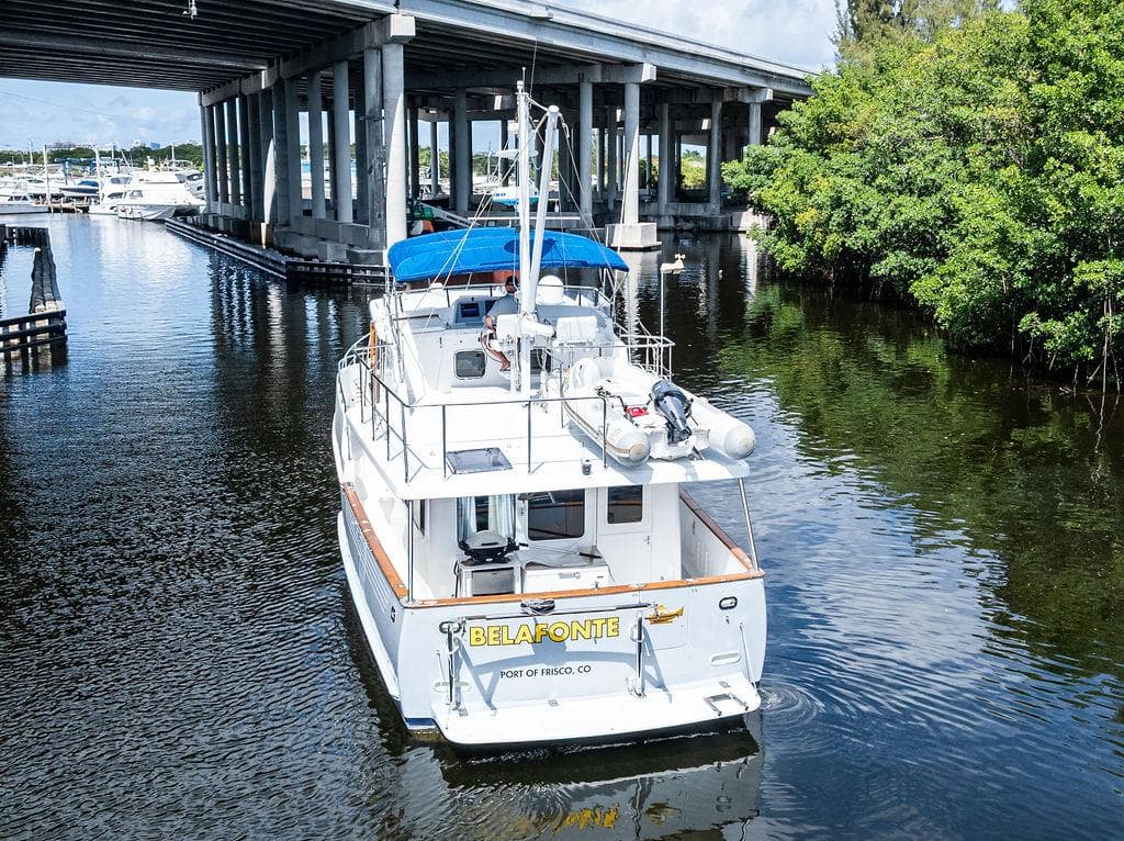 Selene Solo 2000 boat under bridge, calm water, lush greenery, blue canopy, rear view.