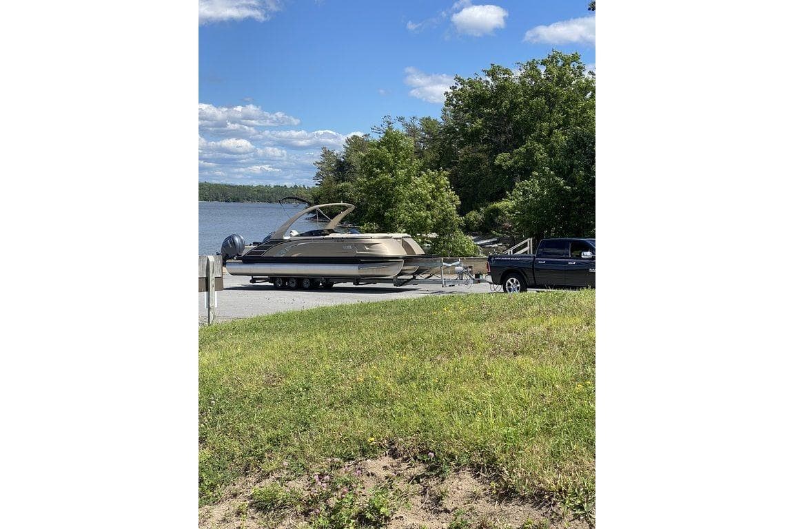 2021 Bennington 27 QXSBWA X2 boat on trailer by a lake, surrounded by trees.