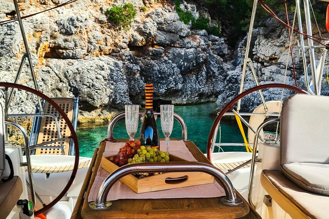 Luxurious Jeanneau Sun Odyssey 50 DS yacht with wine and grapes, scenic rocky cove backdrop.