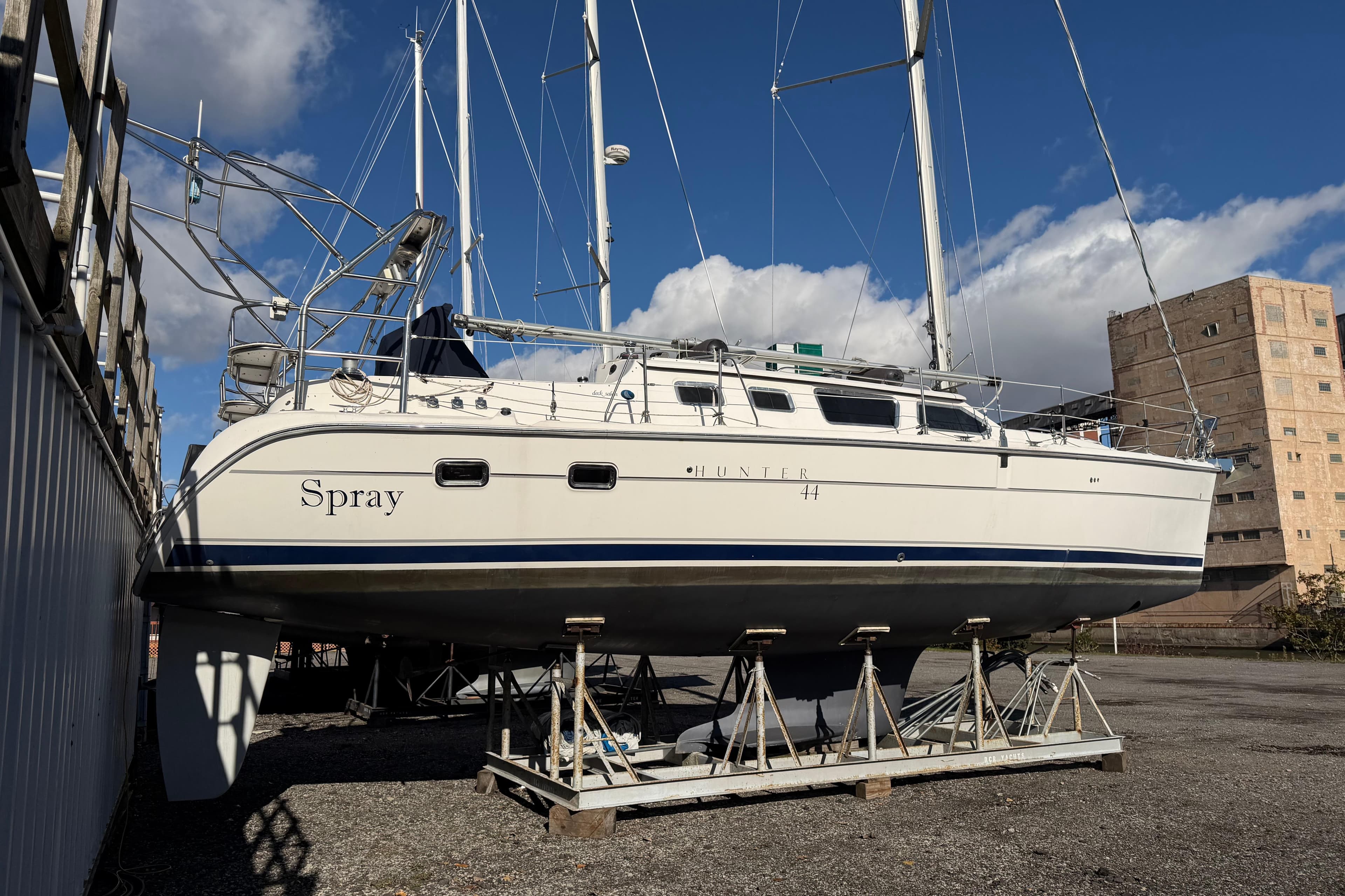 2003 Hunter 44 Deck Salon sailboat named "Spray" on dry dock under blue sky.