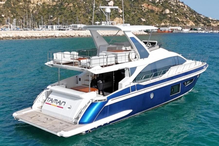 2021 Azimut 66 yacht cruising in clear blue waters near a rocky coastline.
