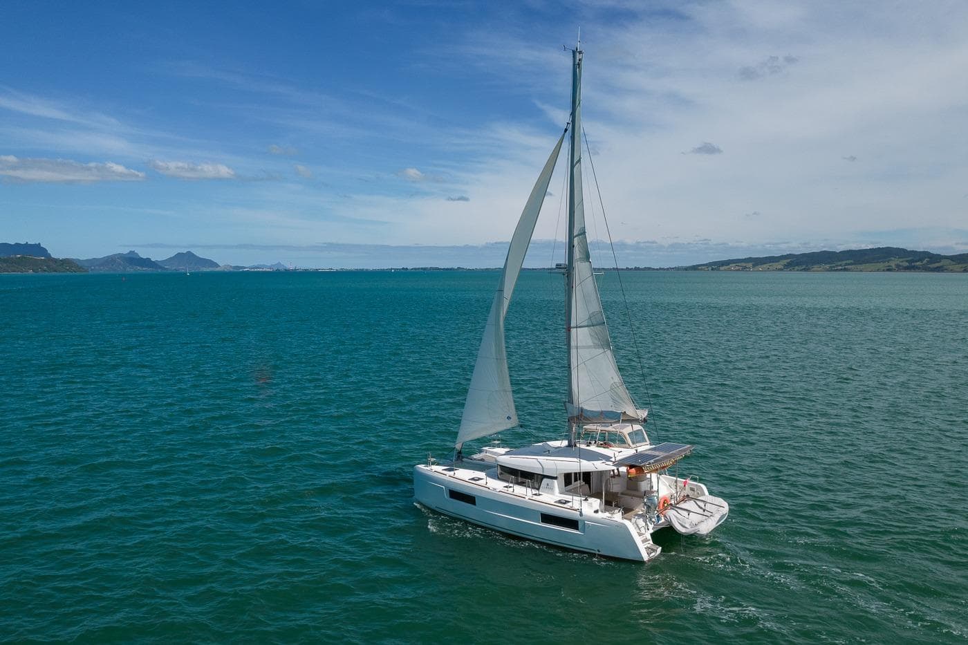 2021 Lagoon 40 catamaran sailing on open sea under clear blue sky.