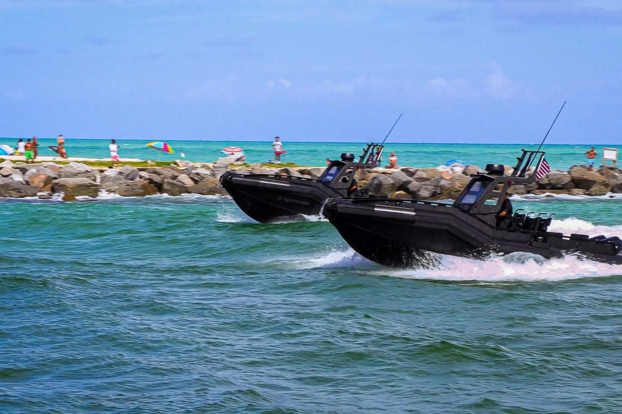 Two DGS 777 military boats speeding near a rocky shoreline, 2022 model.
