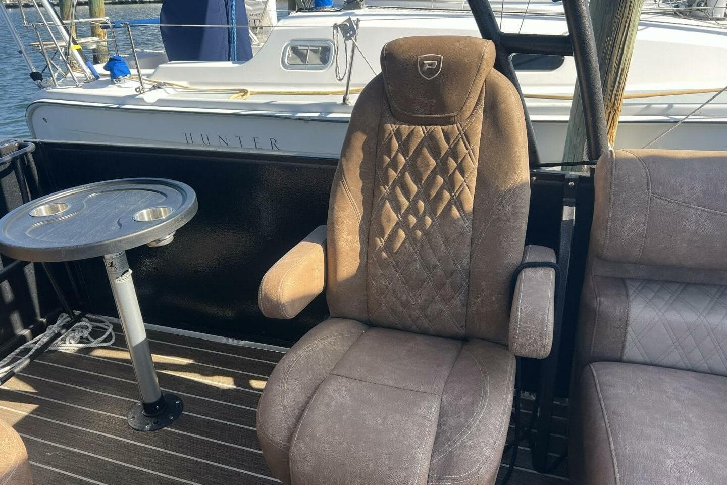 Luxurious seating on 2023 Premier 330 Escalante boat with table, docked near sailboat.