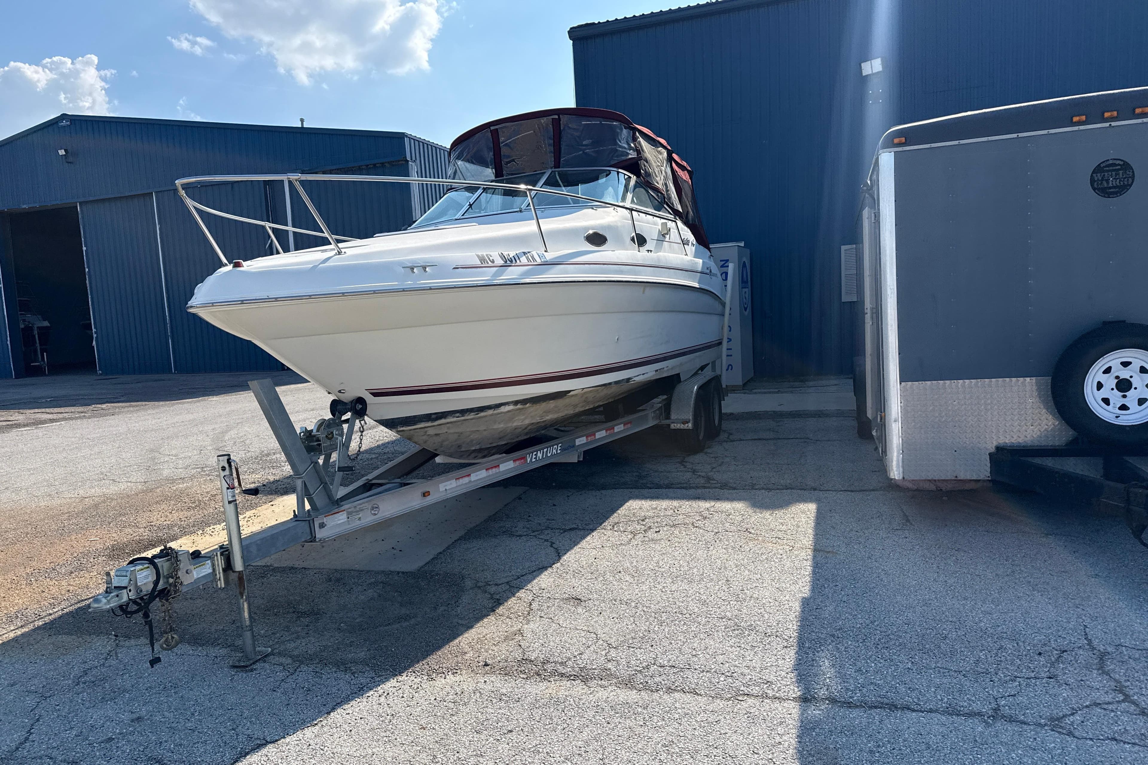 1996 Sea Ray 240 Sundancer boat on trailer, parked near industrial buildings under a clear sky.