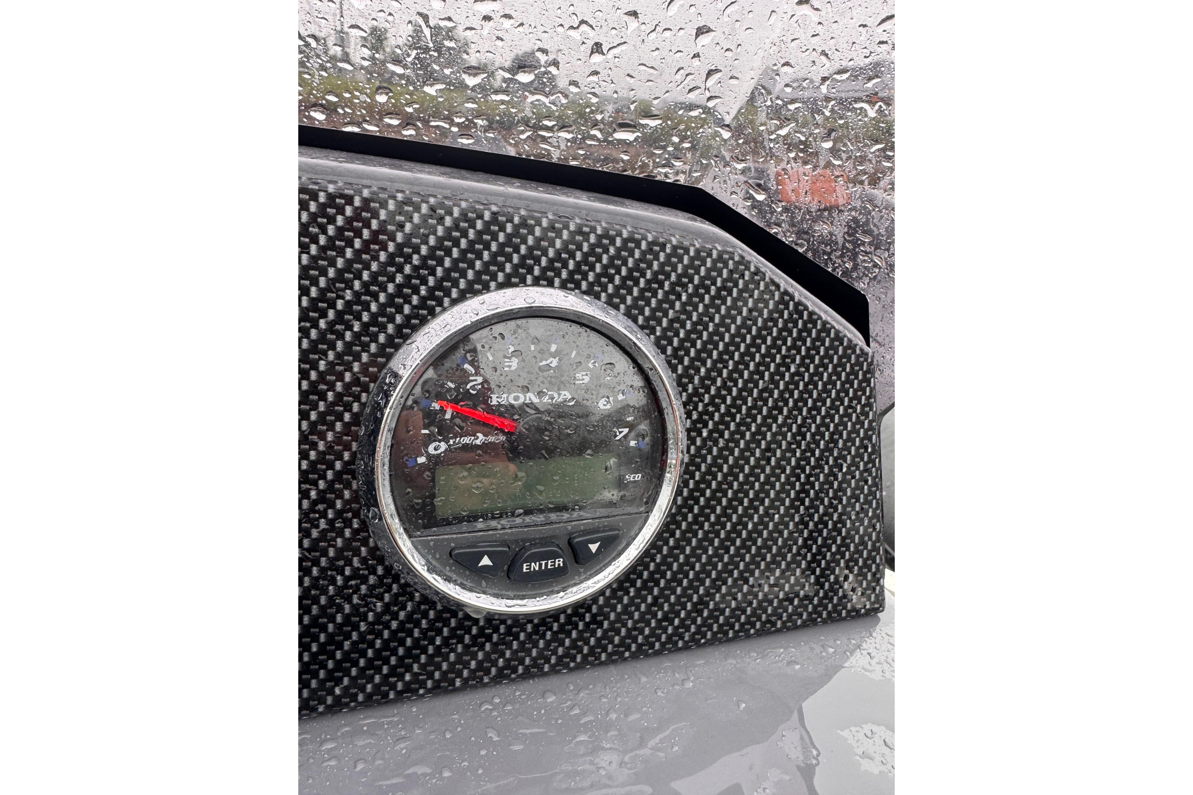 Carbon fiber dashboard with Honda gauge in 2024 Northstar Axis 4.8, rain-covered.