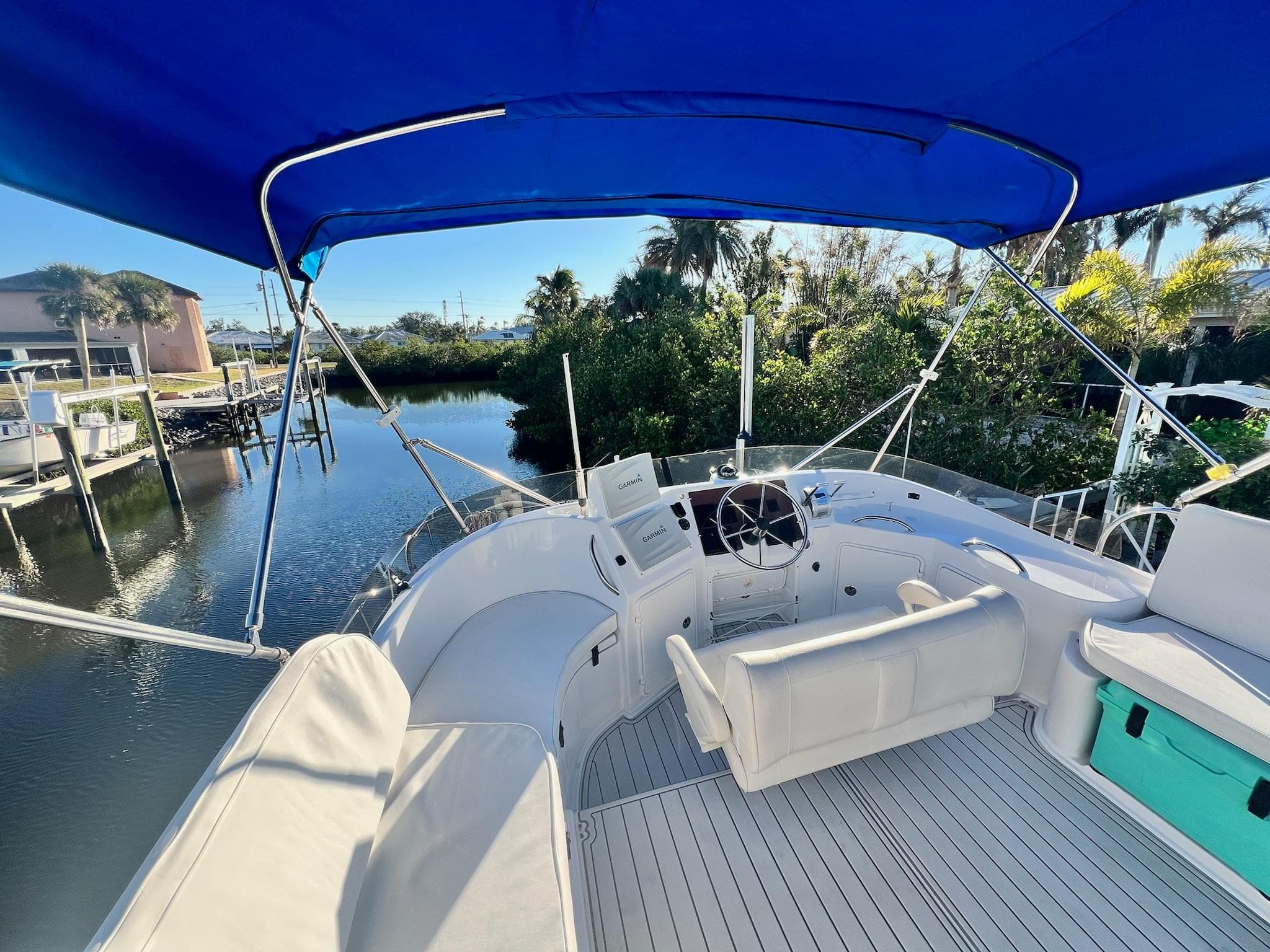2006 PDQ MV34 boat with blue canopy, docked near lush greenery.