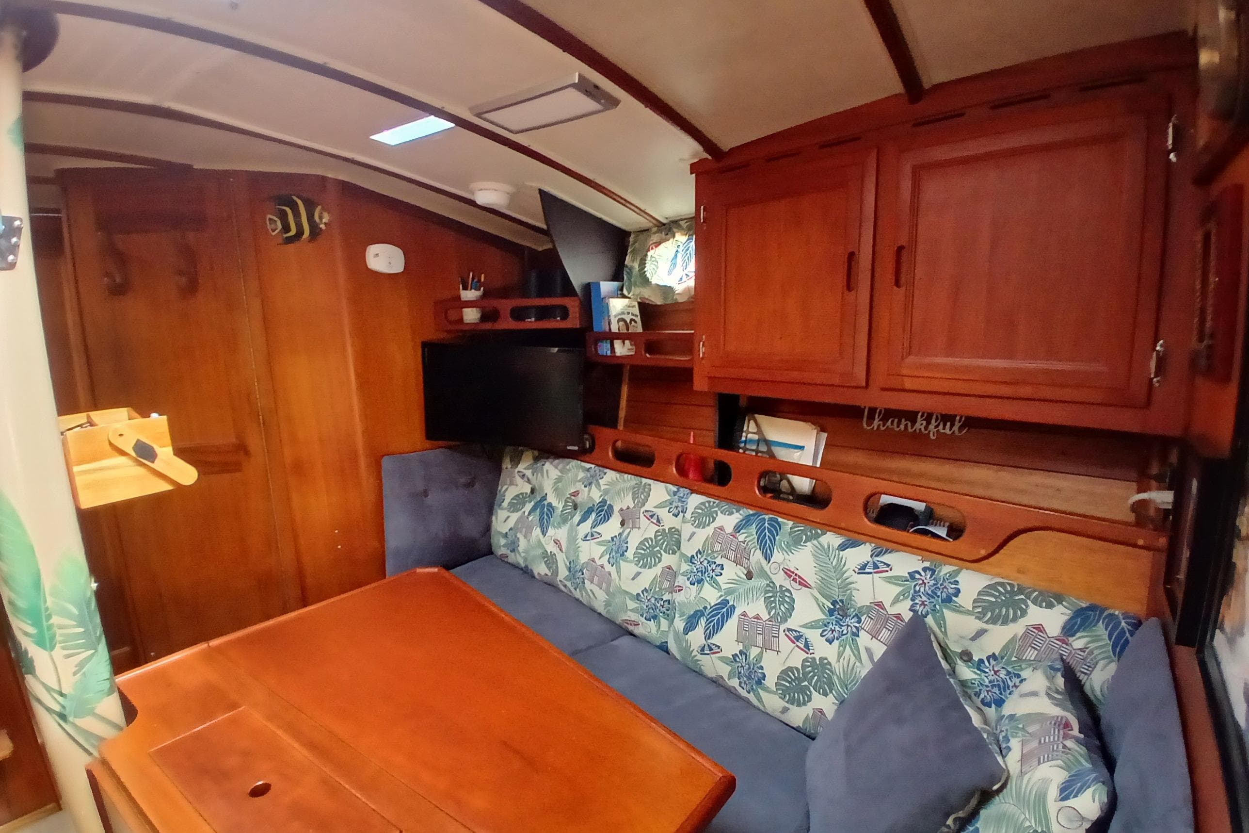 Cozy interior of a 1977 Ericson 36 C sailboat with wooden cabinetry and floral upholstery.