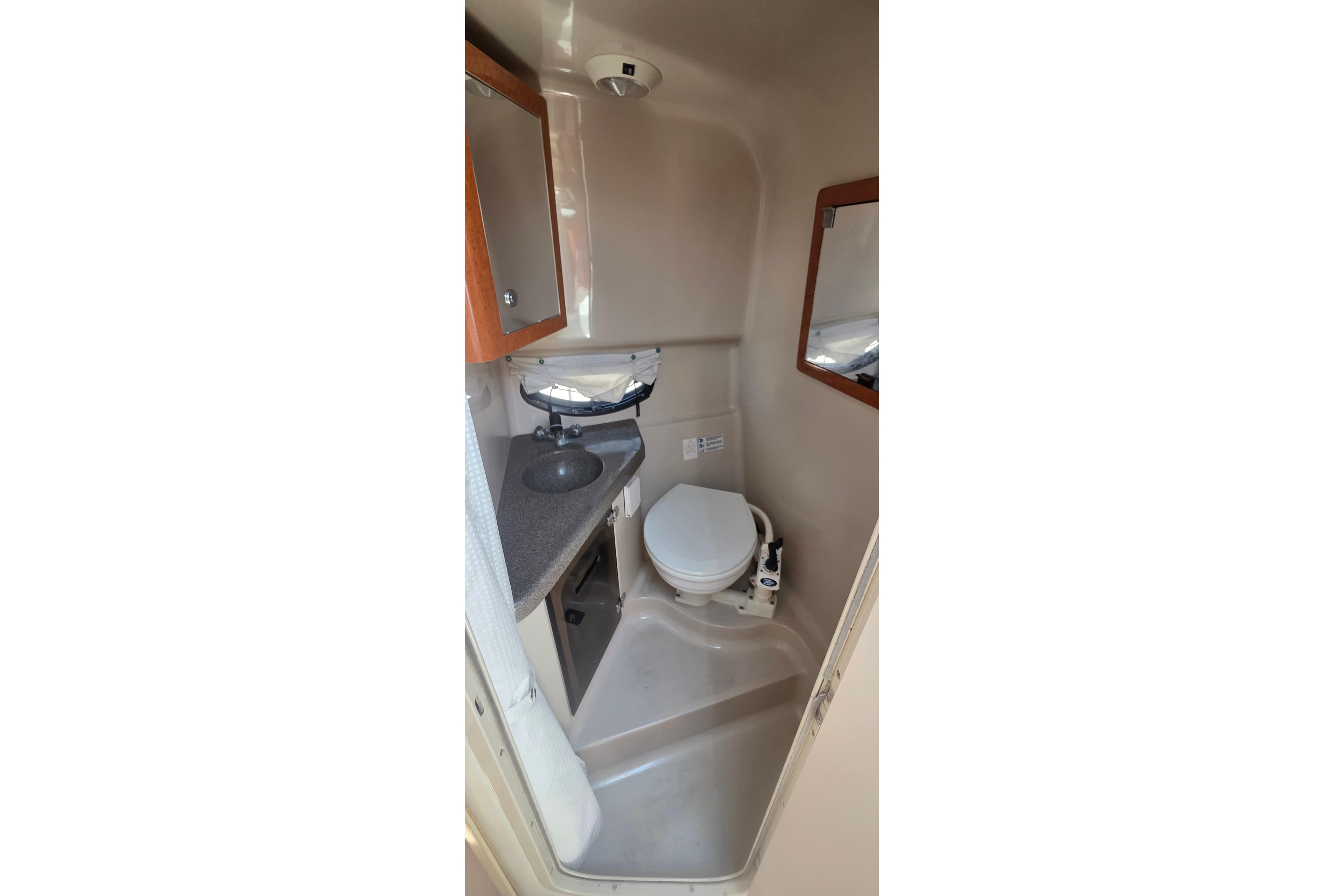Compact bathroom in a 2001 Doral 250se boat, featuring a toilet, sink, and mirror.