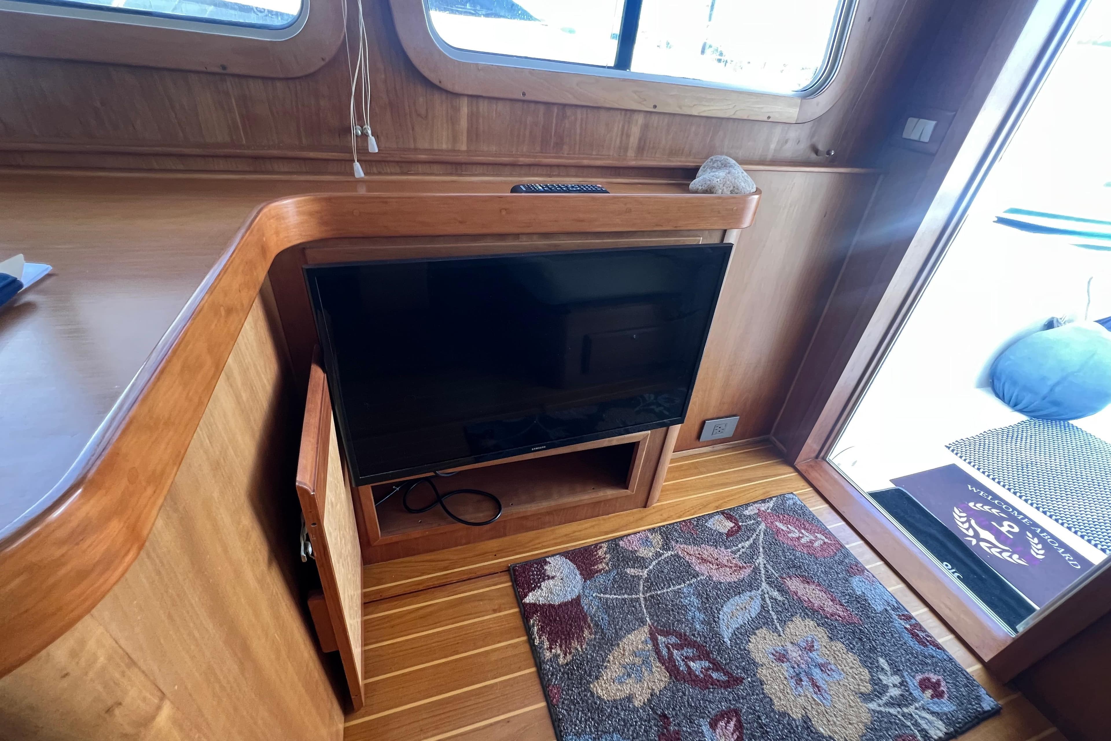 Interior of 2005 Sabre Flybridge yacht with TV, wooden cabinetry, and floral rug.