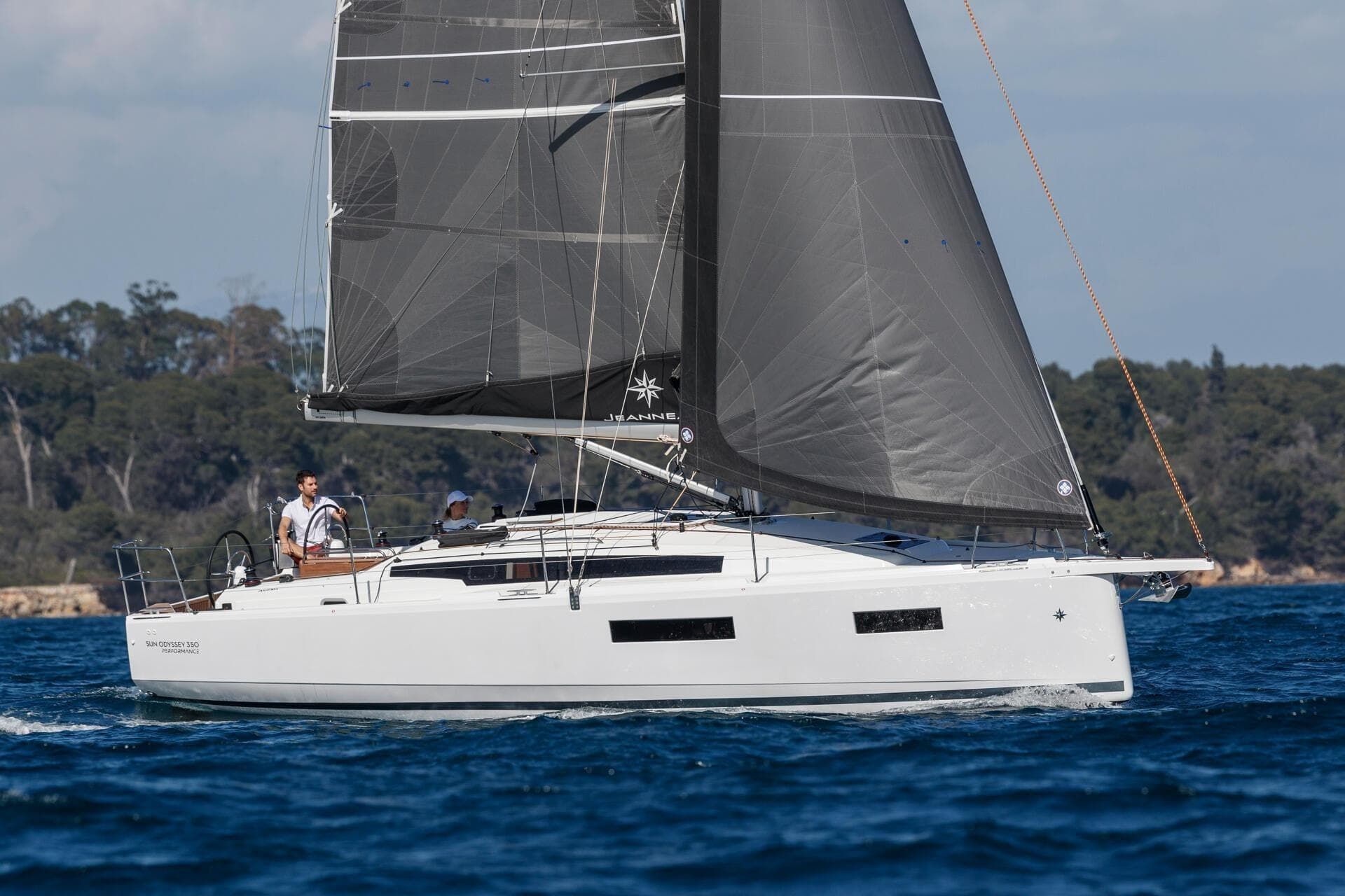 2026 Jeanneau Sun Odyssey 350 sailing on blue waters with lush green shoreline.