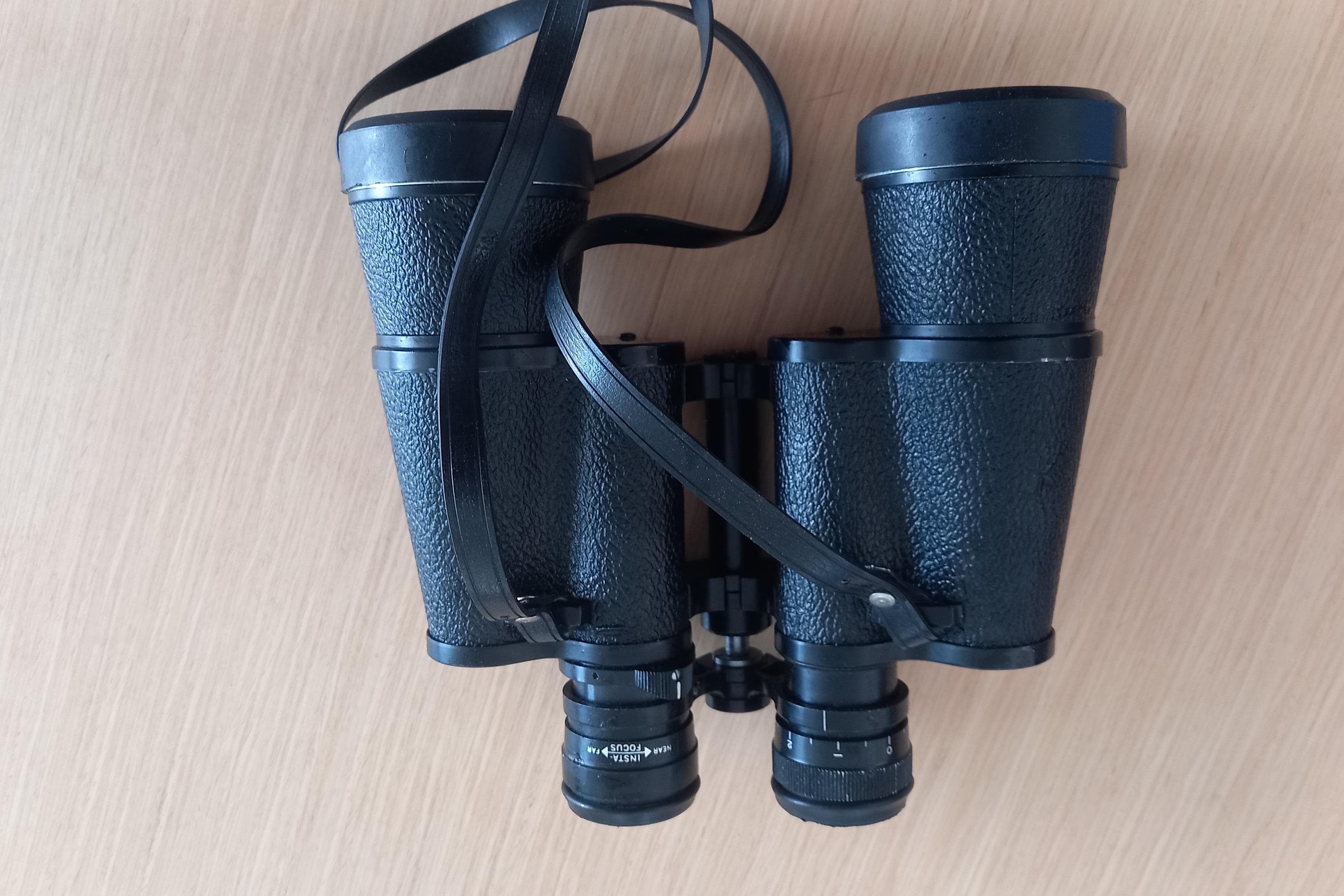 Black binoculars with textured grip and strap on a wooden surface.