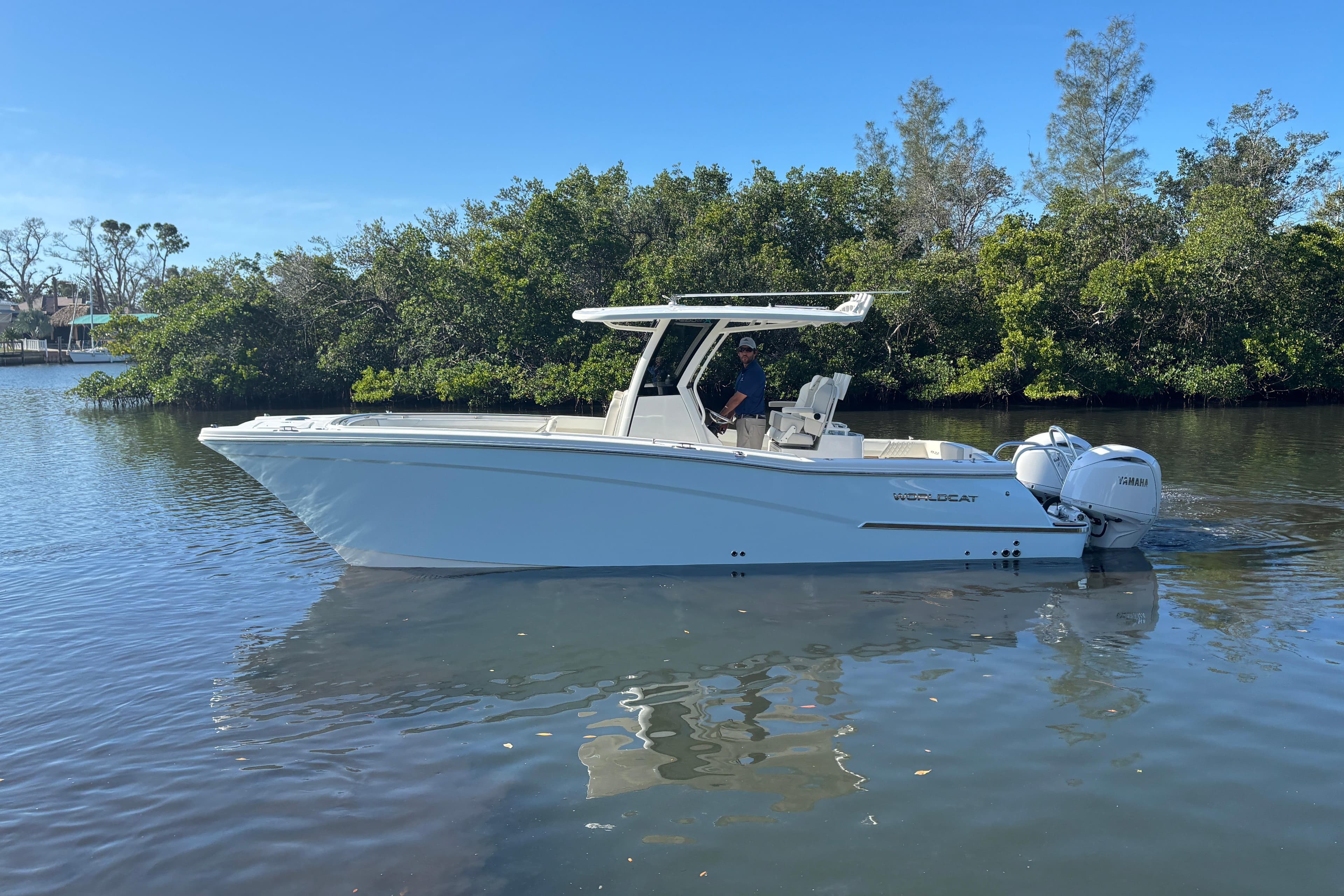 2026 World Cat 280 CC-X boat cruising on calm water near lush greenery.