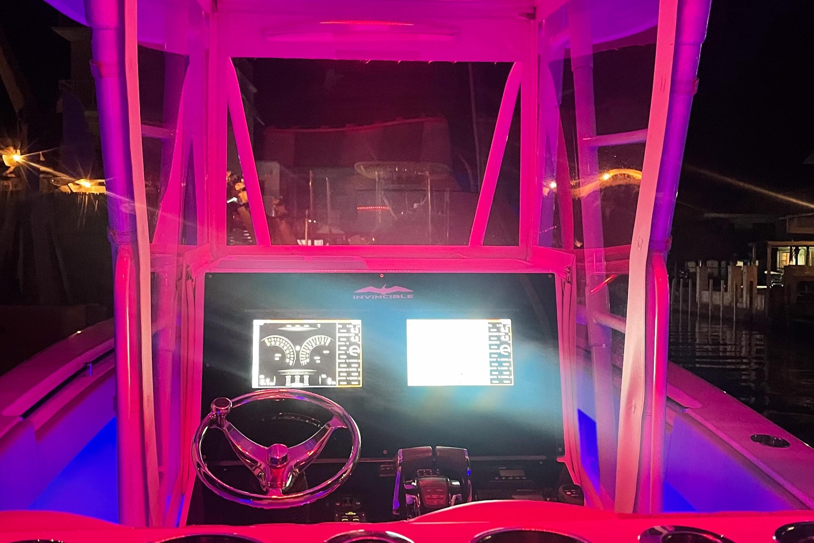 Cockpit of 2008 Invincible 33 boat illuminated with vibrant pink lighting at night.
