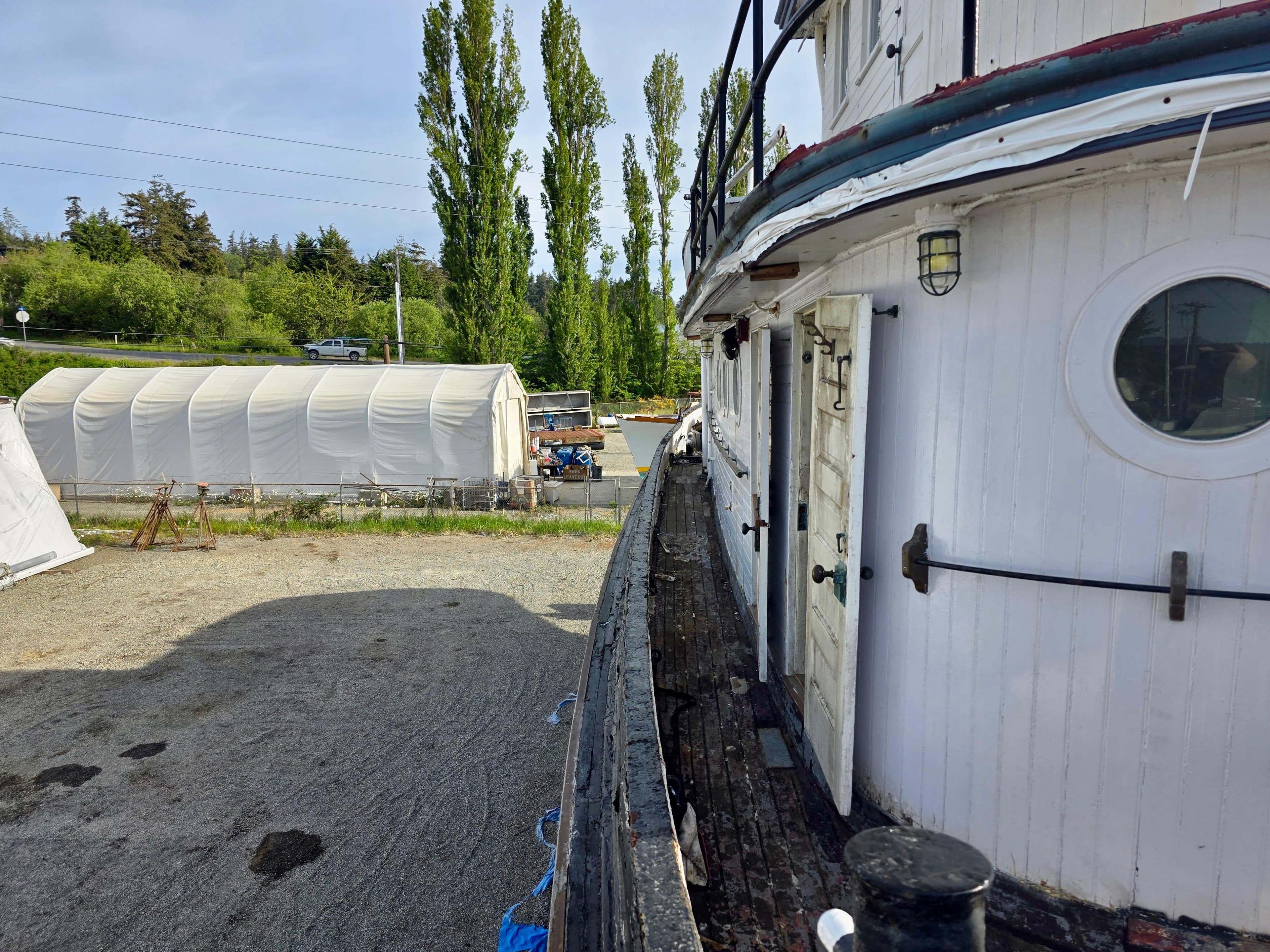 Historic 1890 custom tugboat docked, surrounded by trees and a white tent structure.