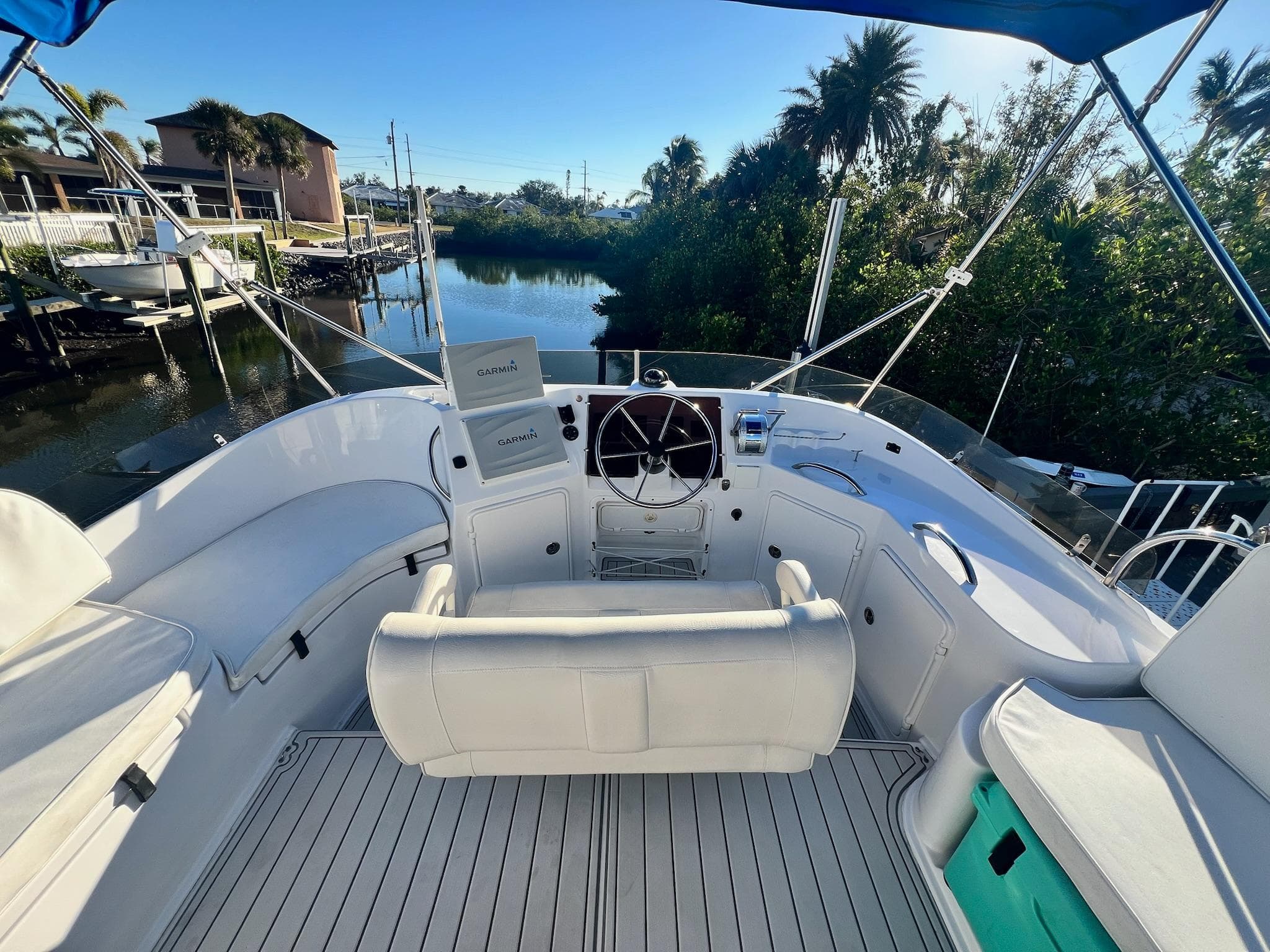 2006 PDQ MV34 boat cockpit with white seating, steering wheel, and lush waterfront view.