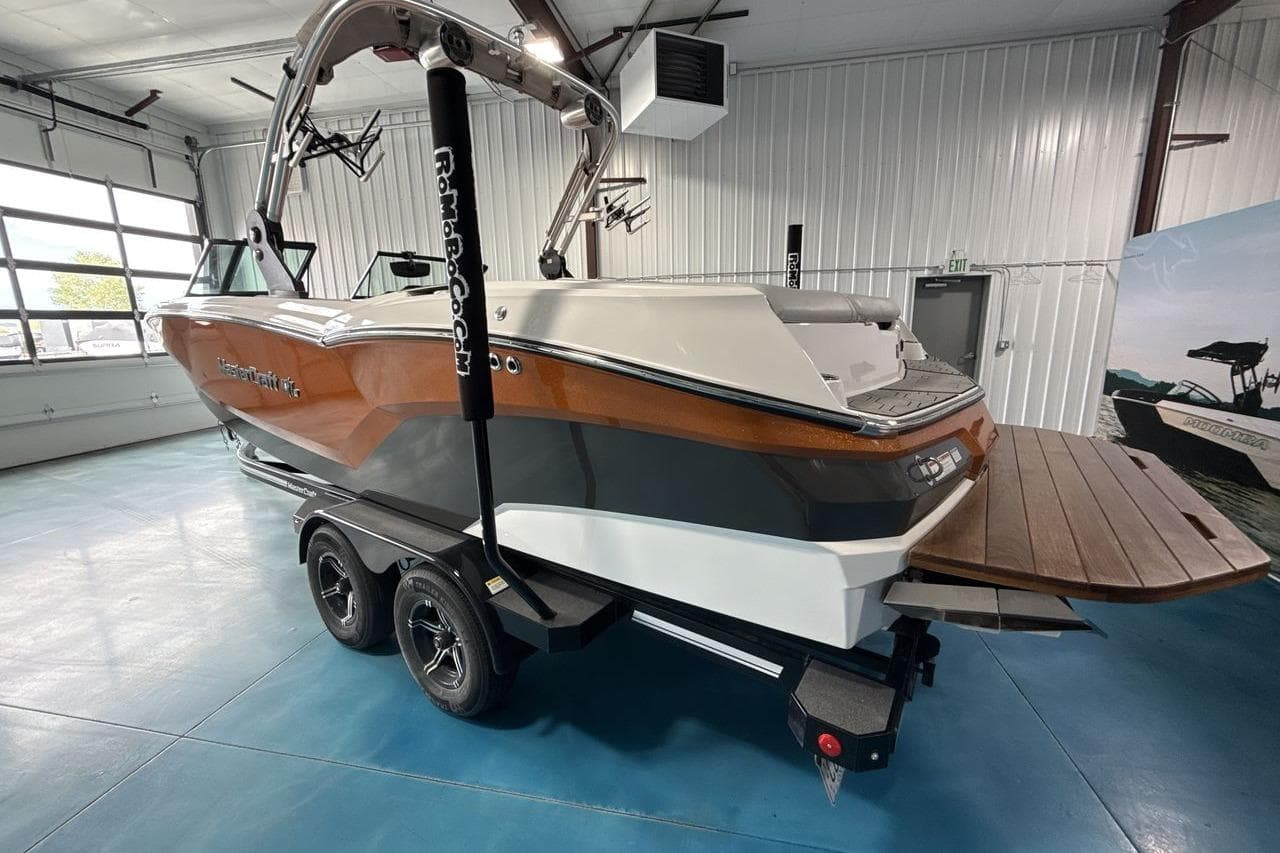 2021 MasterCraft NXT24 boat in showroom, featuring sleek design and dual-axle trailer.