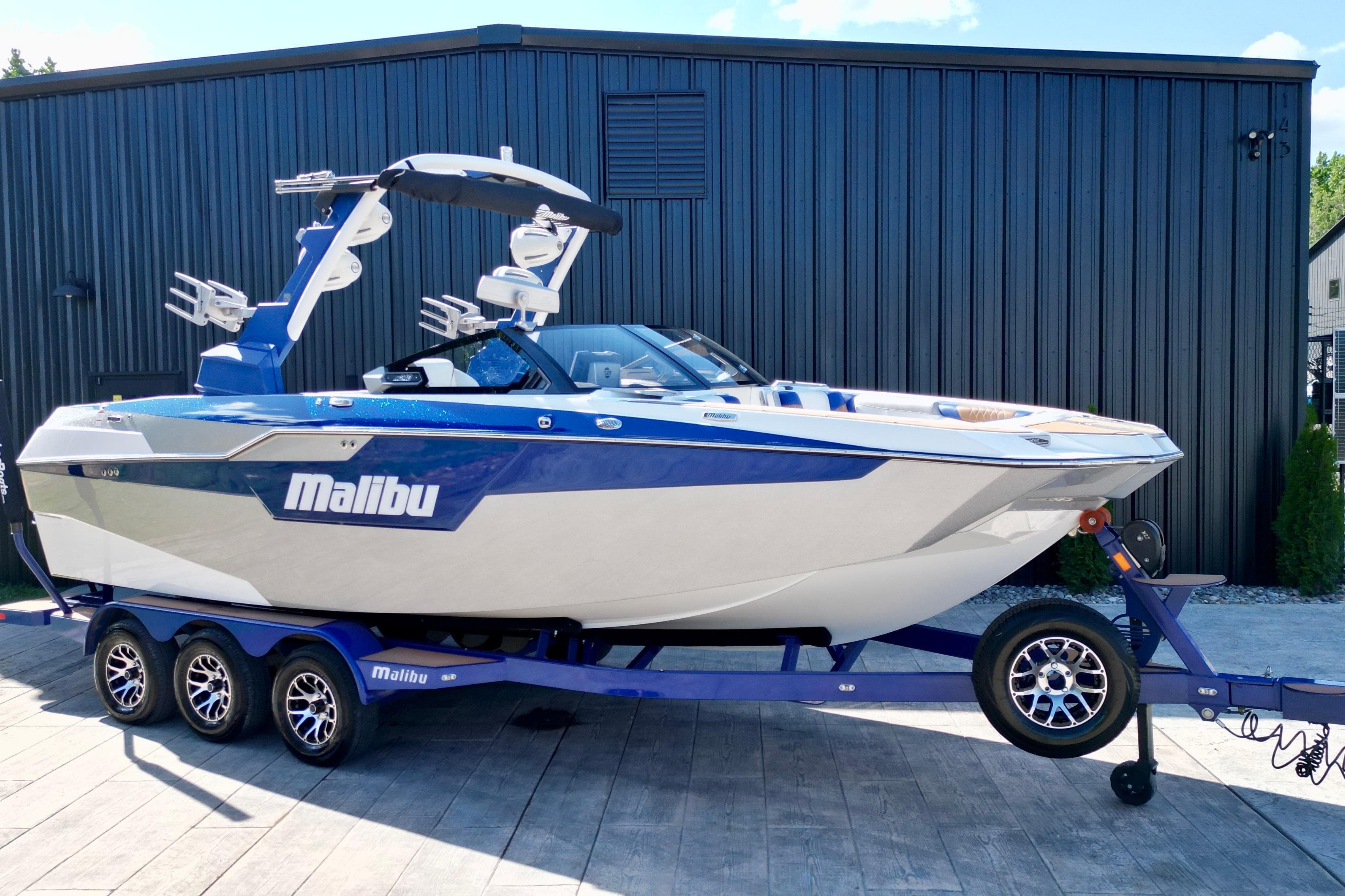 2022 Malibu M240 boat on trailer, blue and white design, parked outdoors.
