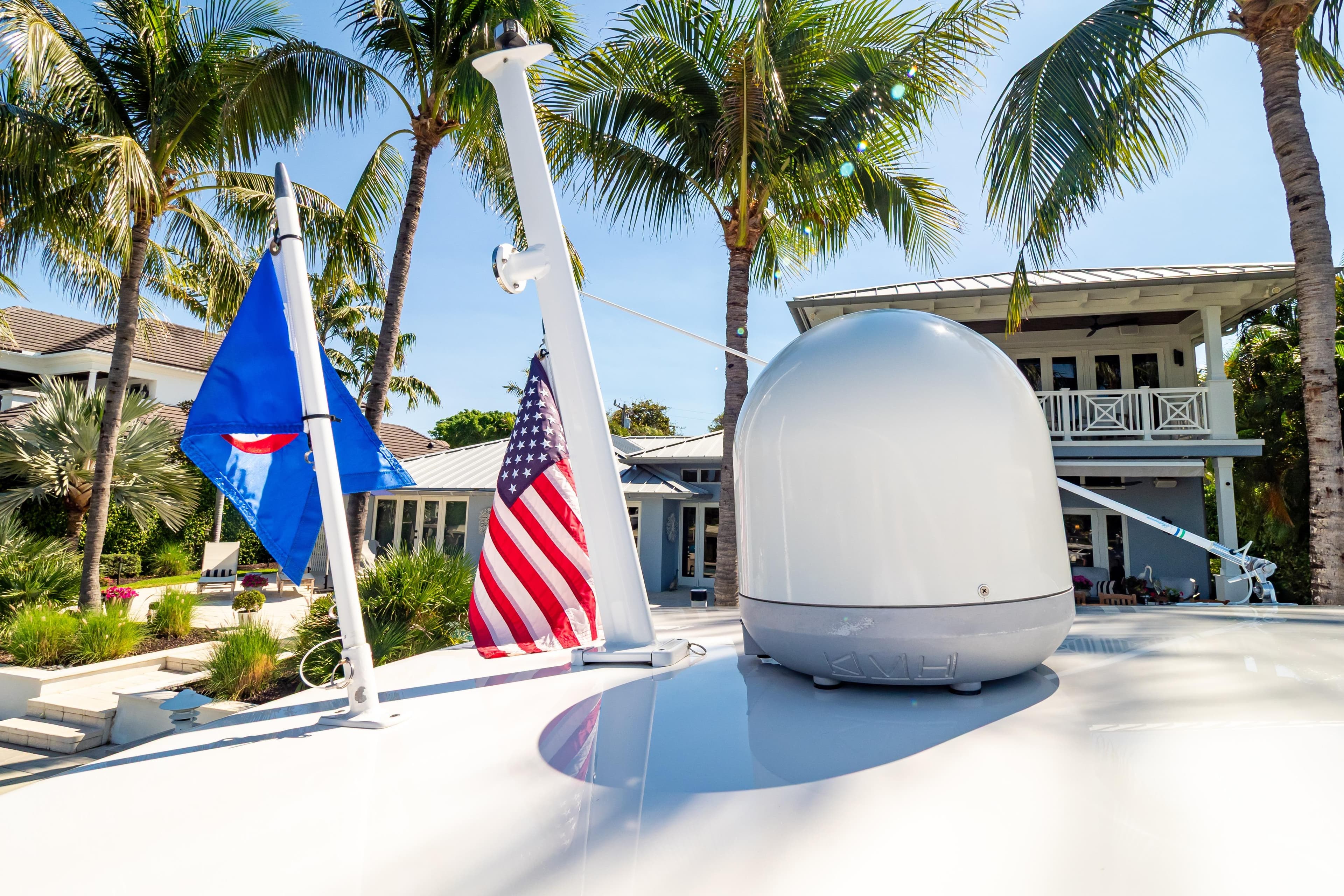 2016 Intrepid 400 Cuddy yacht with flags, palm trees, and a modern house in the background.
