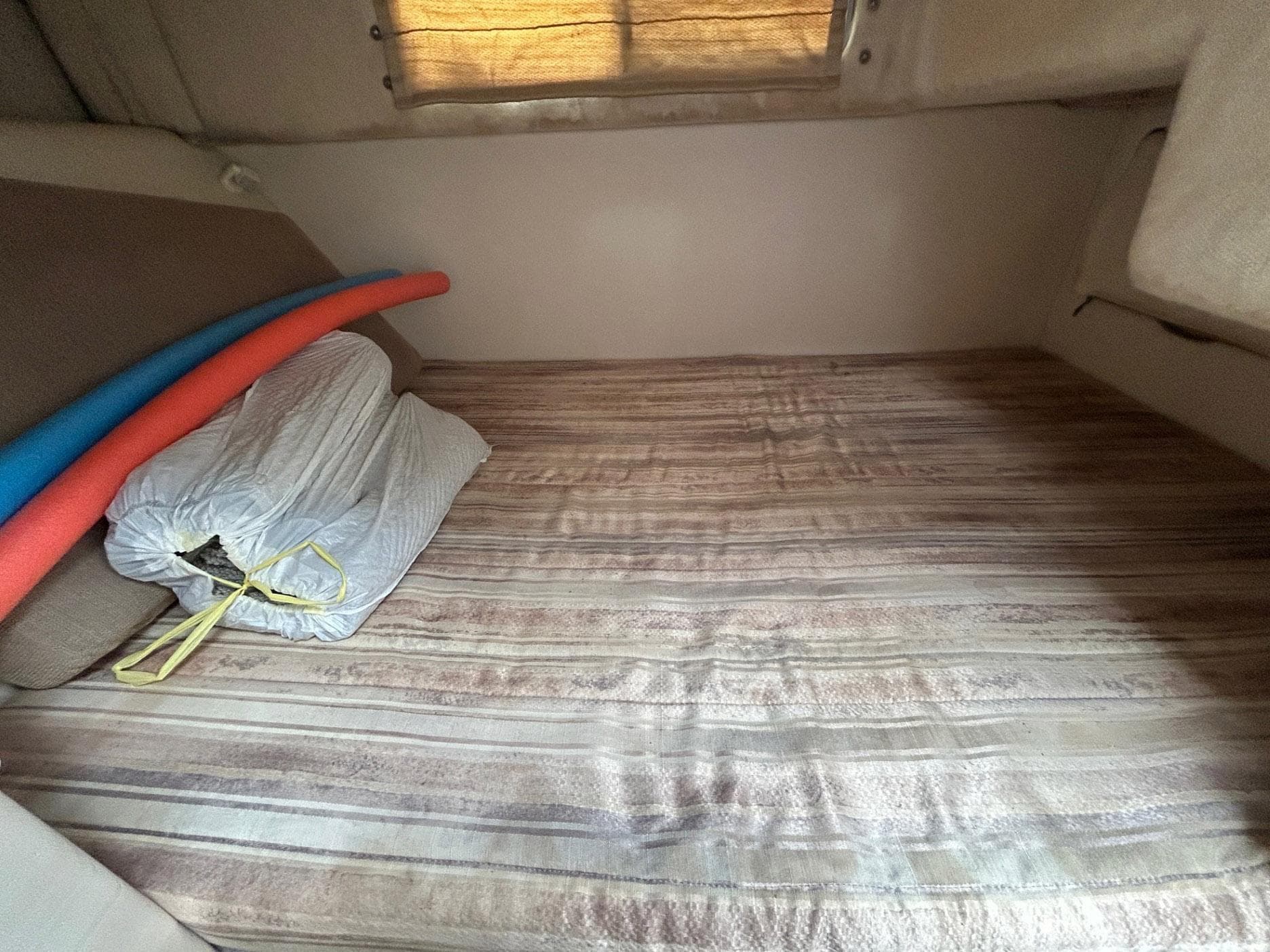 Interior cabin of 1998 Maxum 2800 SCR boat with striped bedding and pool noodles.