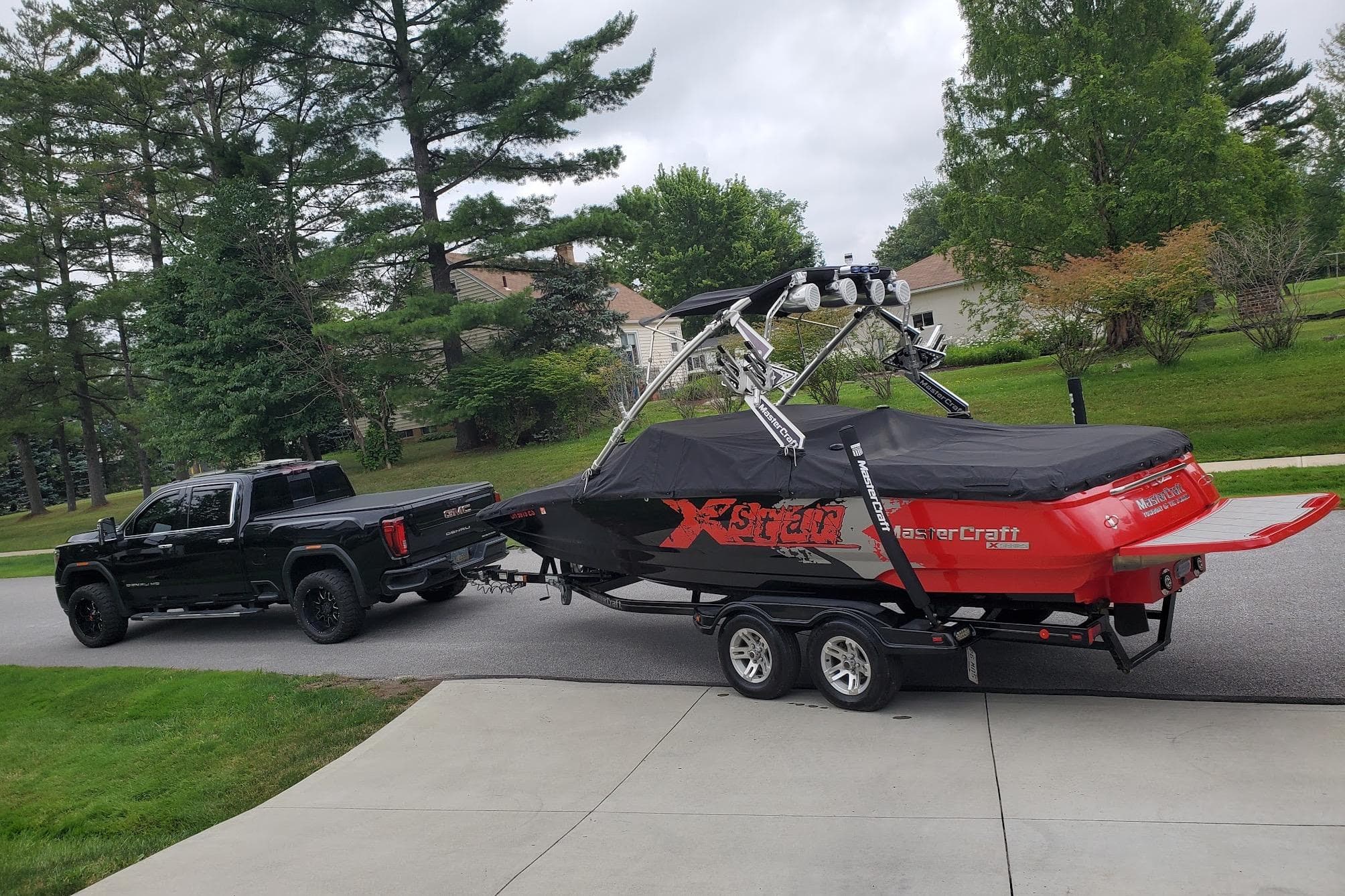 Black truck towing a 2008 MasterCraft XStar 23 boat on a suburban street.