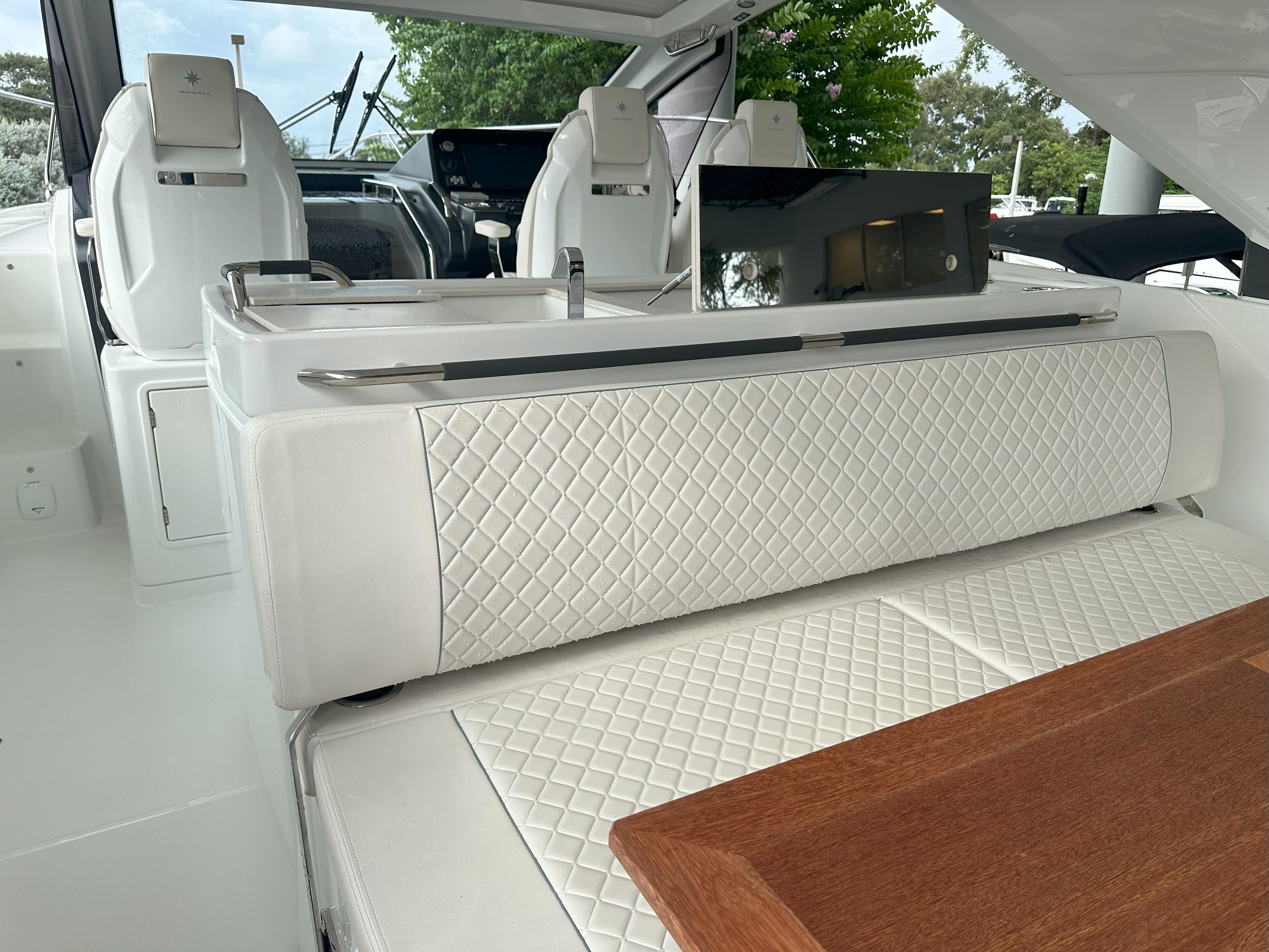 2024 Jeanneau DB 43 interior with white quilted seating and wooden table.