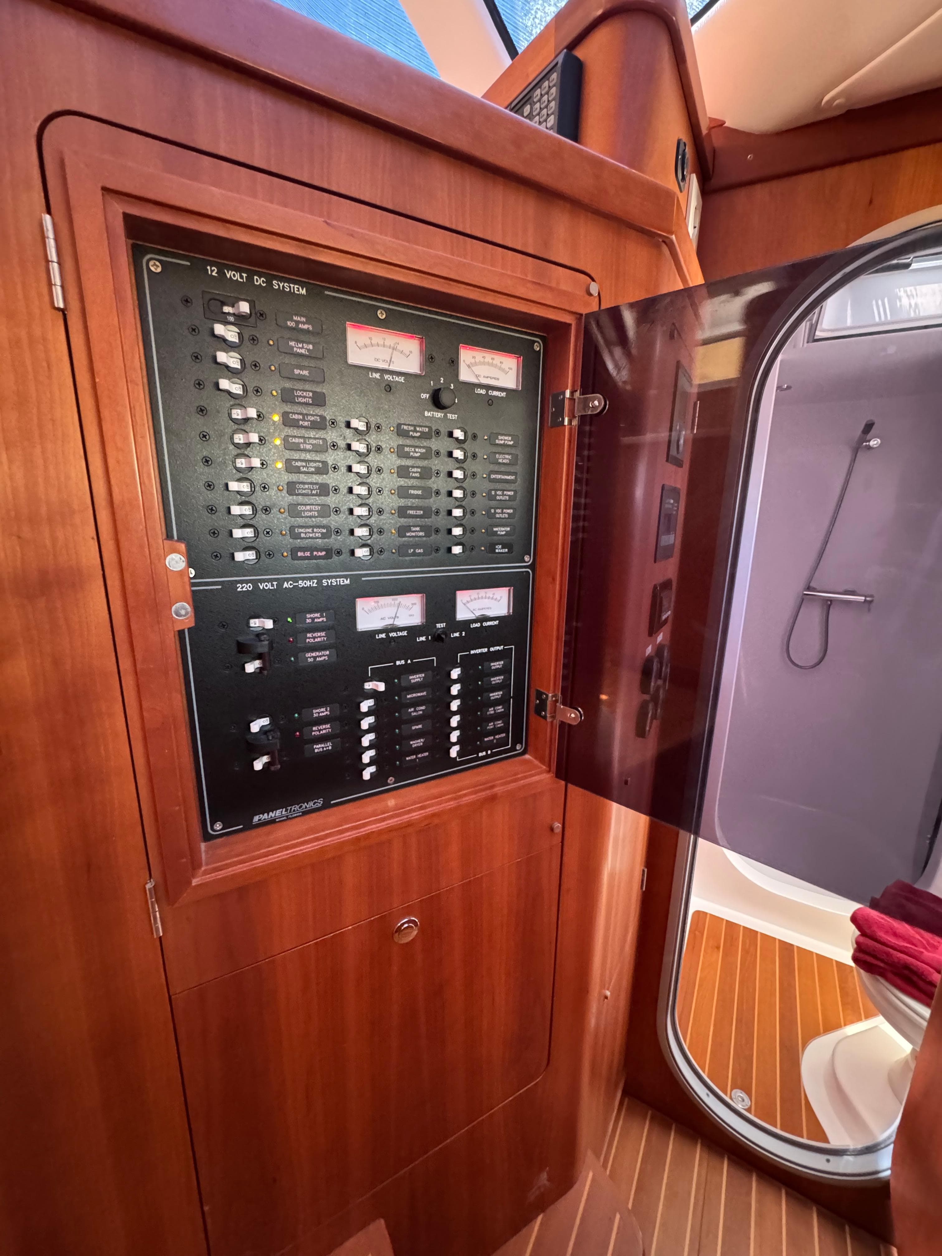 Electrical panel inside 2016 Antares 44 yacht, featuring wooden cabinetry and adjacent bathroom.