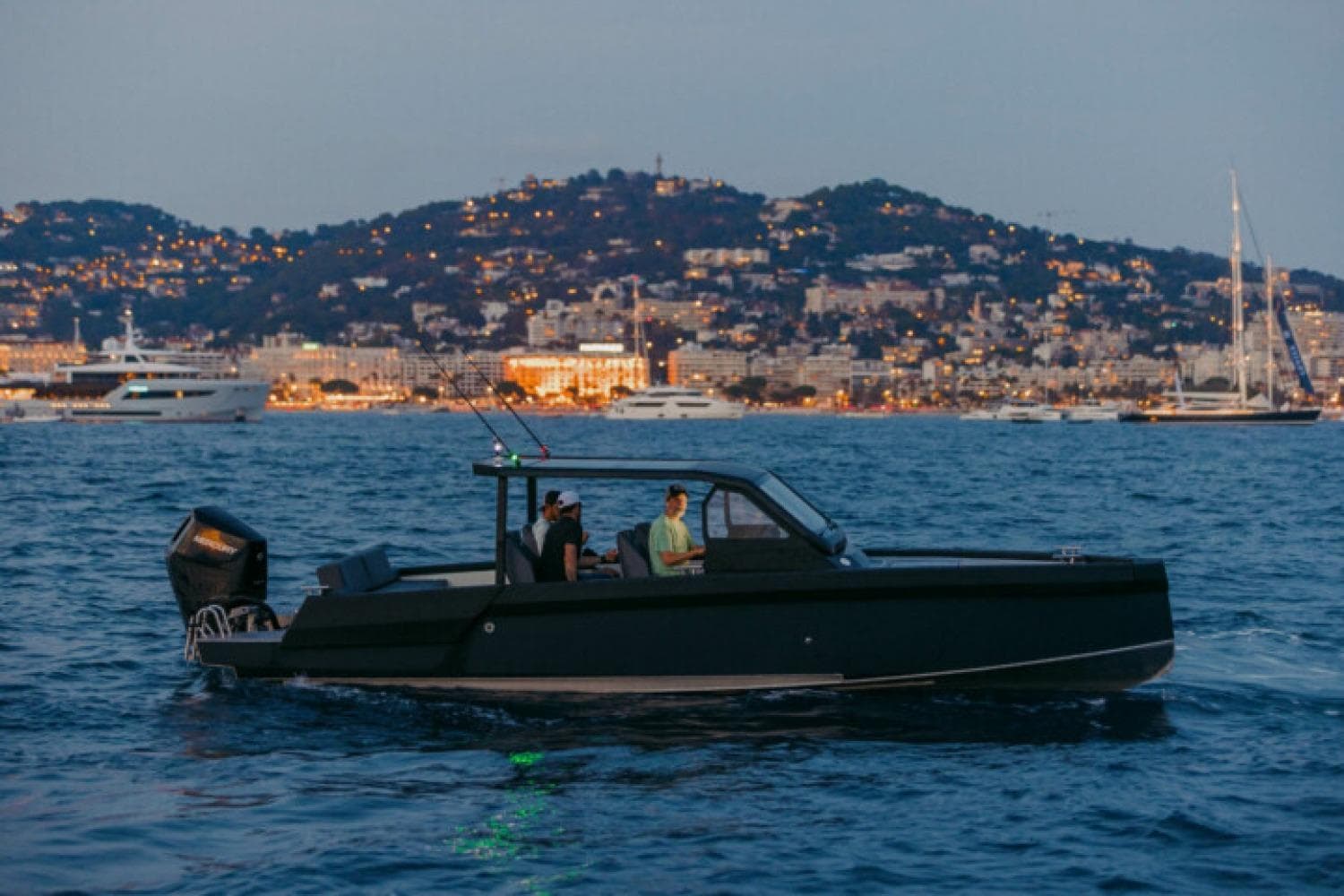 Modern XO DFNDR 8 boat cruising at dusk near a lit coastal city, 2027 model.