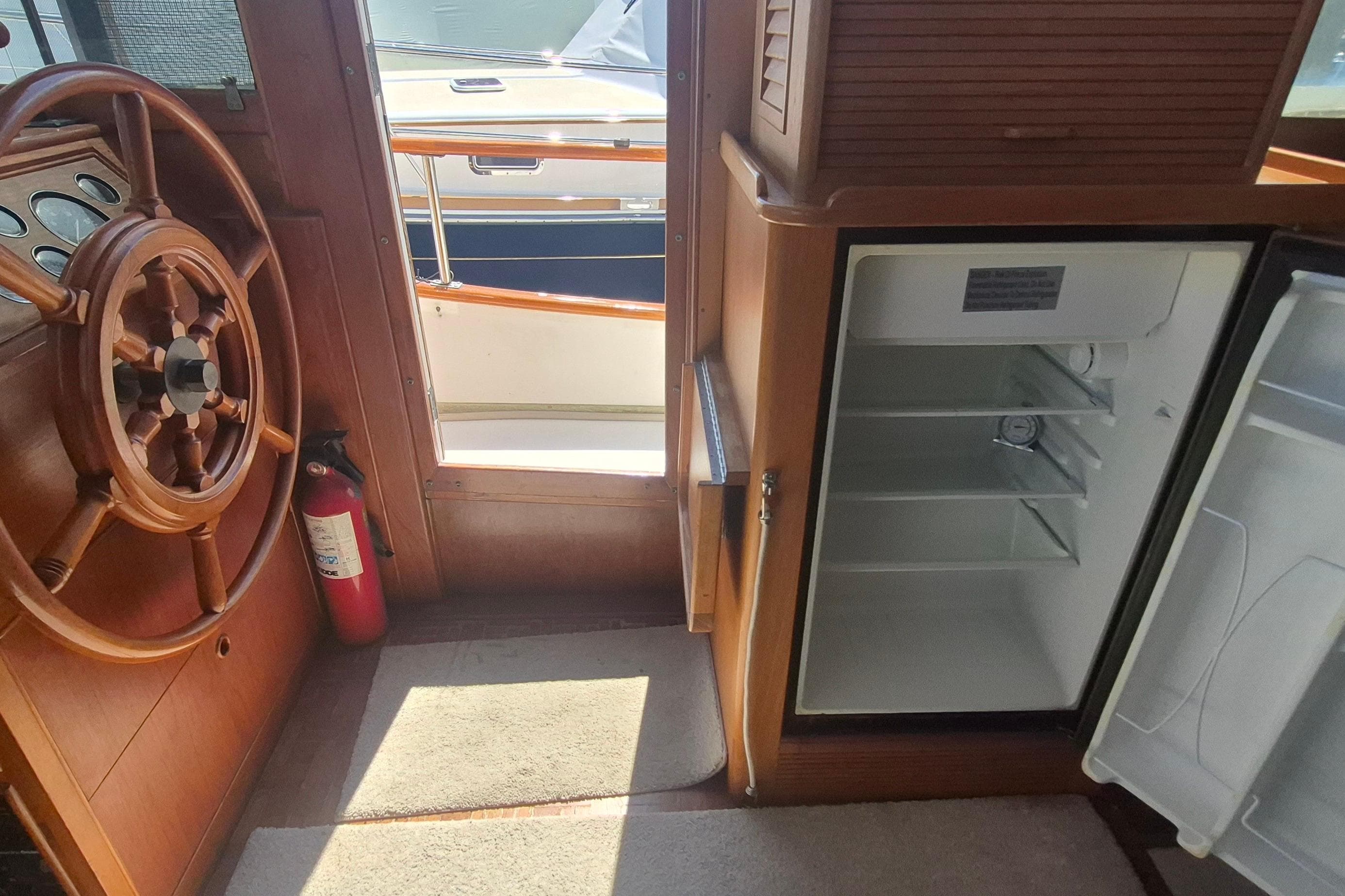 Interior of 1983 Grand Banks 42 Motoryacht with wooden helm and open fridge.