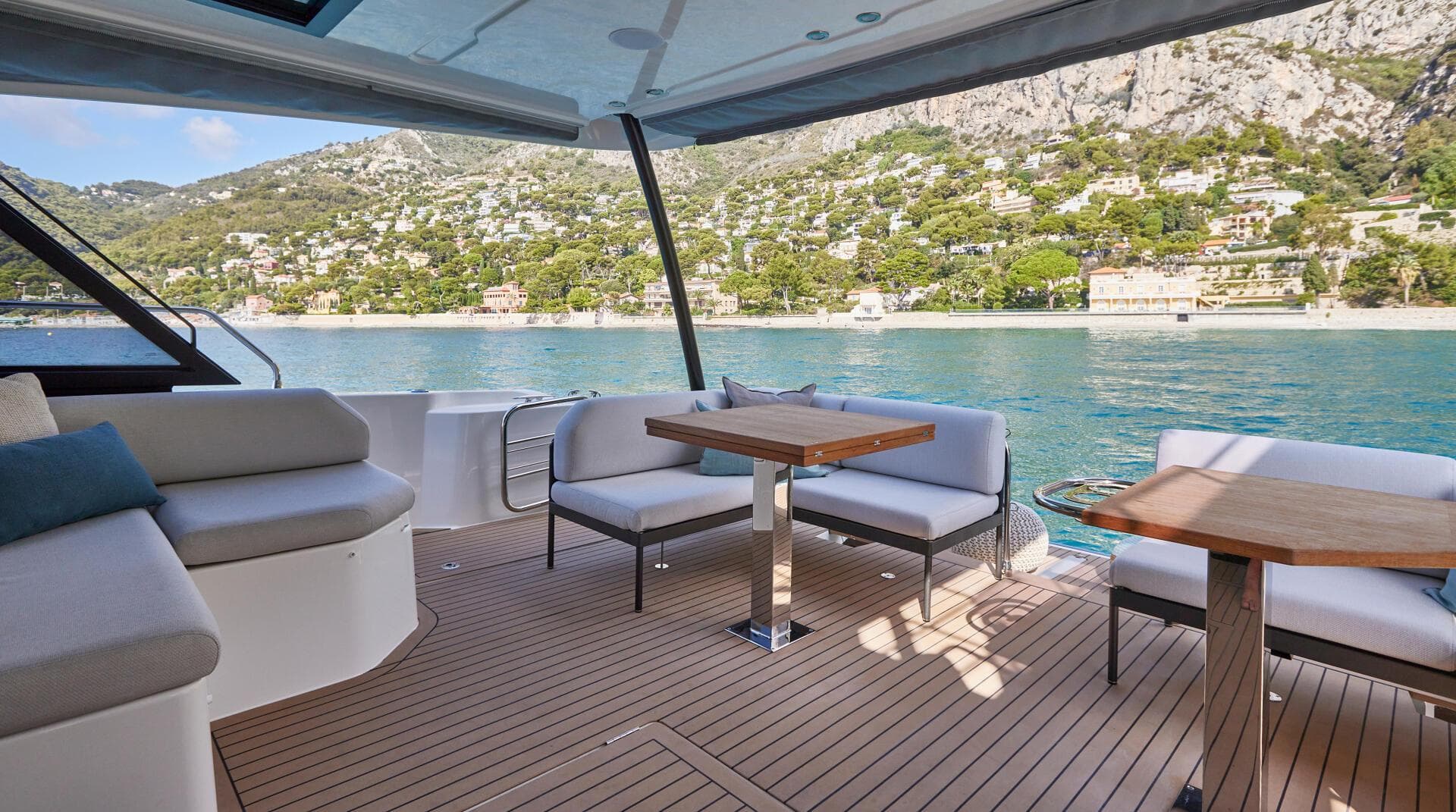 Prestige M48 2025 yacht deck with seating and tables, overlooking scenic coastal view.