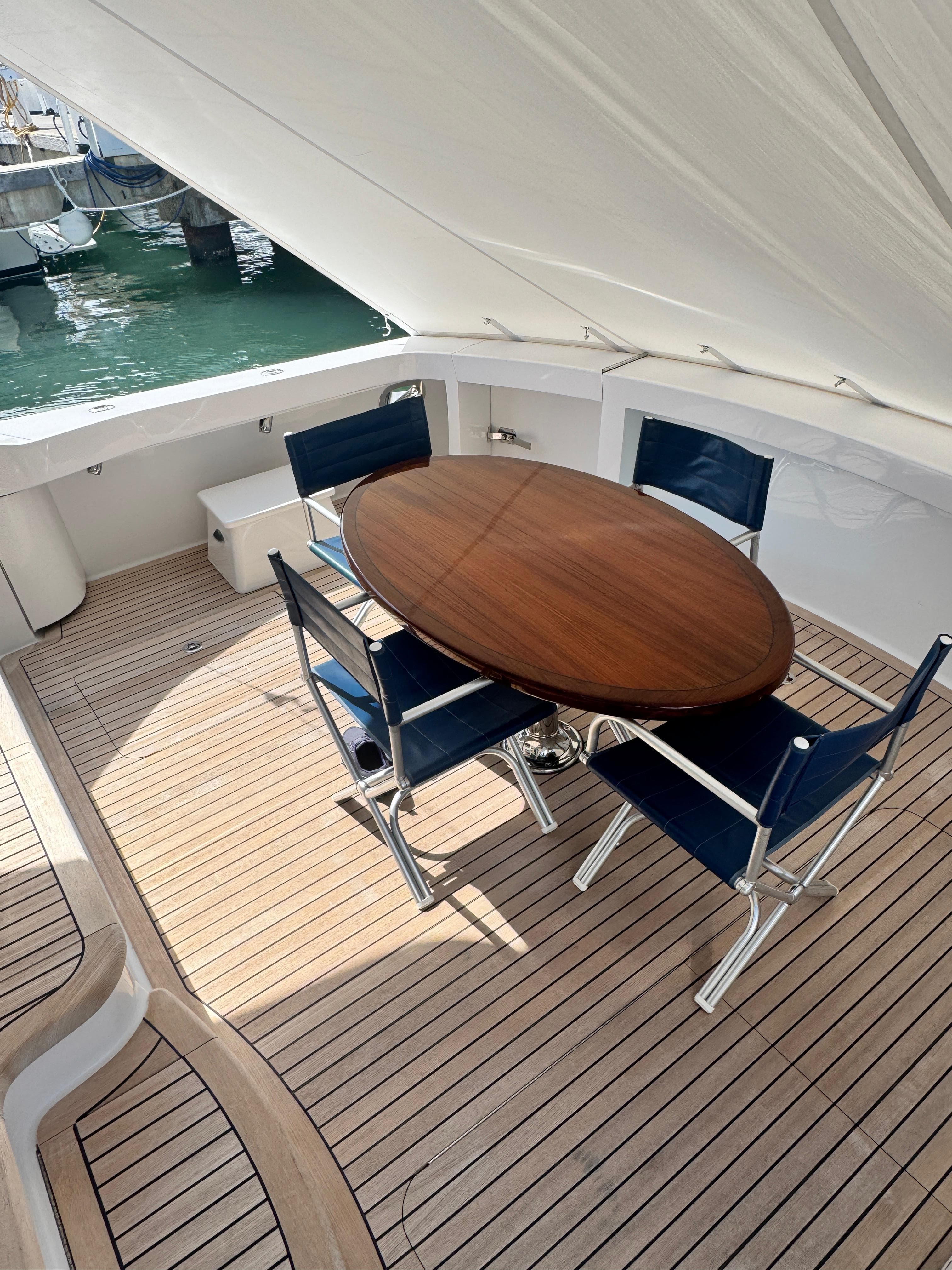Outdoor seating area on 2011 Hatteras GT60 yacht with wooden table and blue chairs.