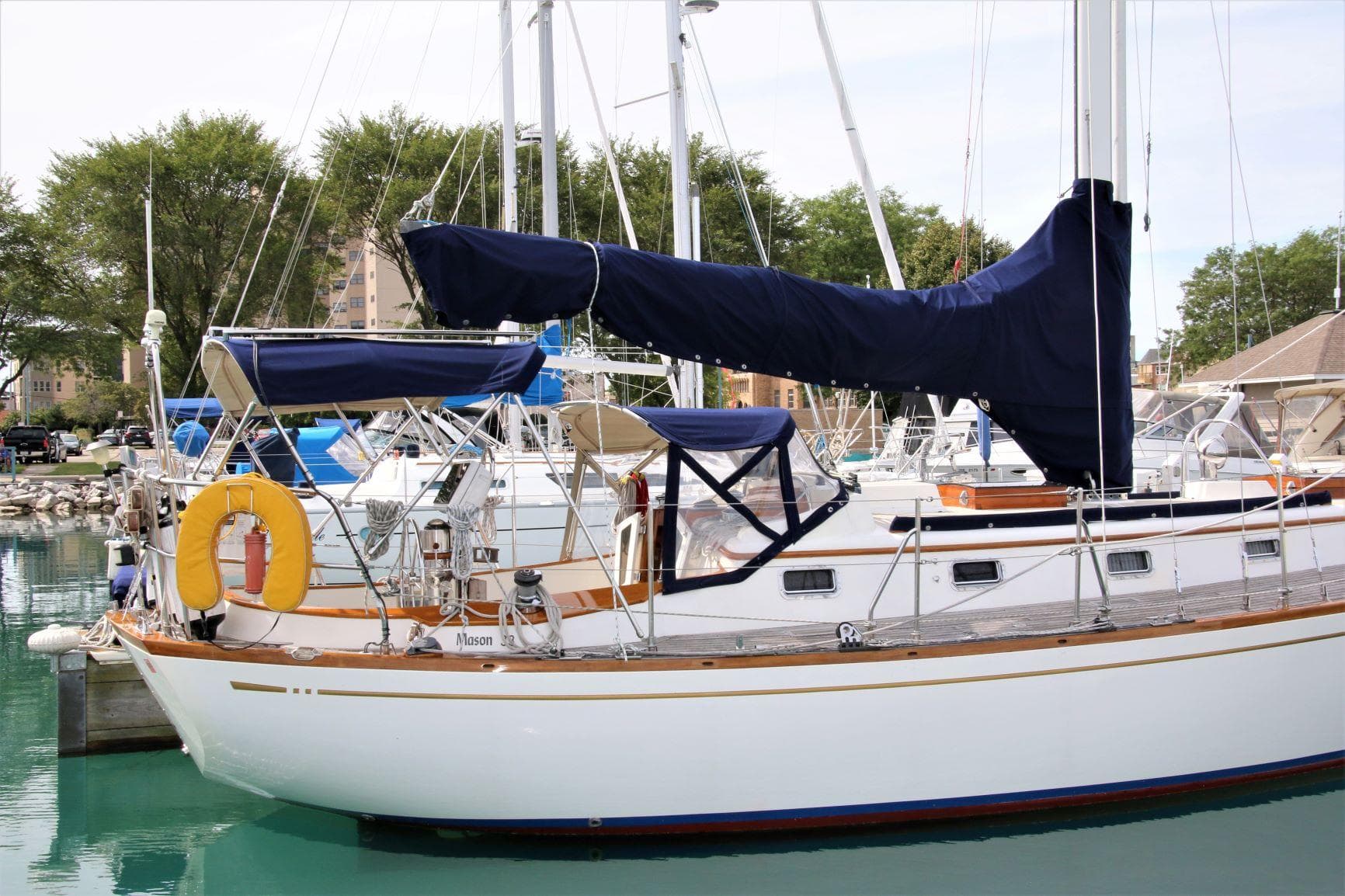 1986 Mason 33 sailboat docked in marina, featuring blue covers and white hull.