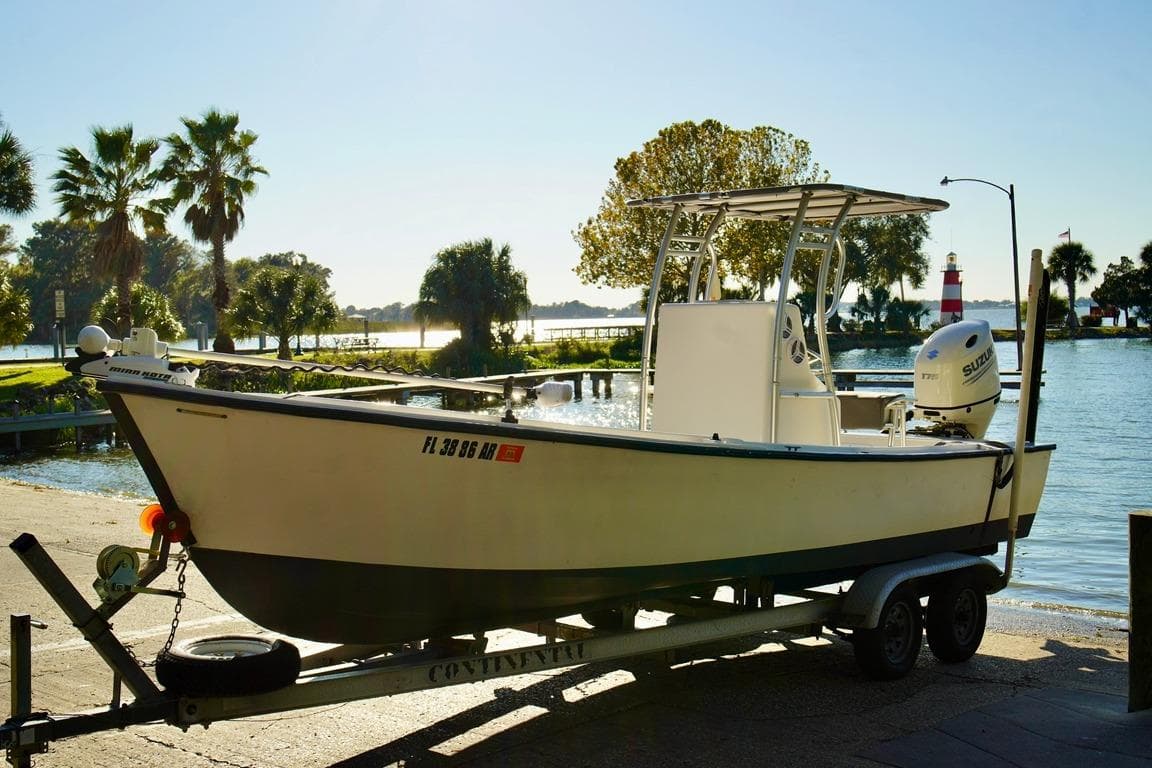 1970 Aquasport 222 Flatback boat on trailer by scenic waterfront with palm trees.