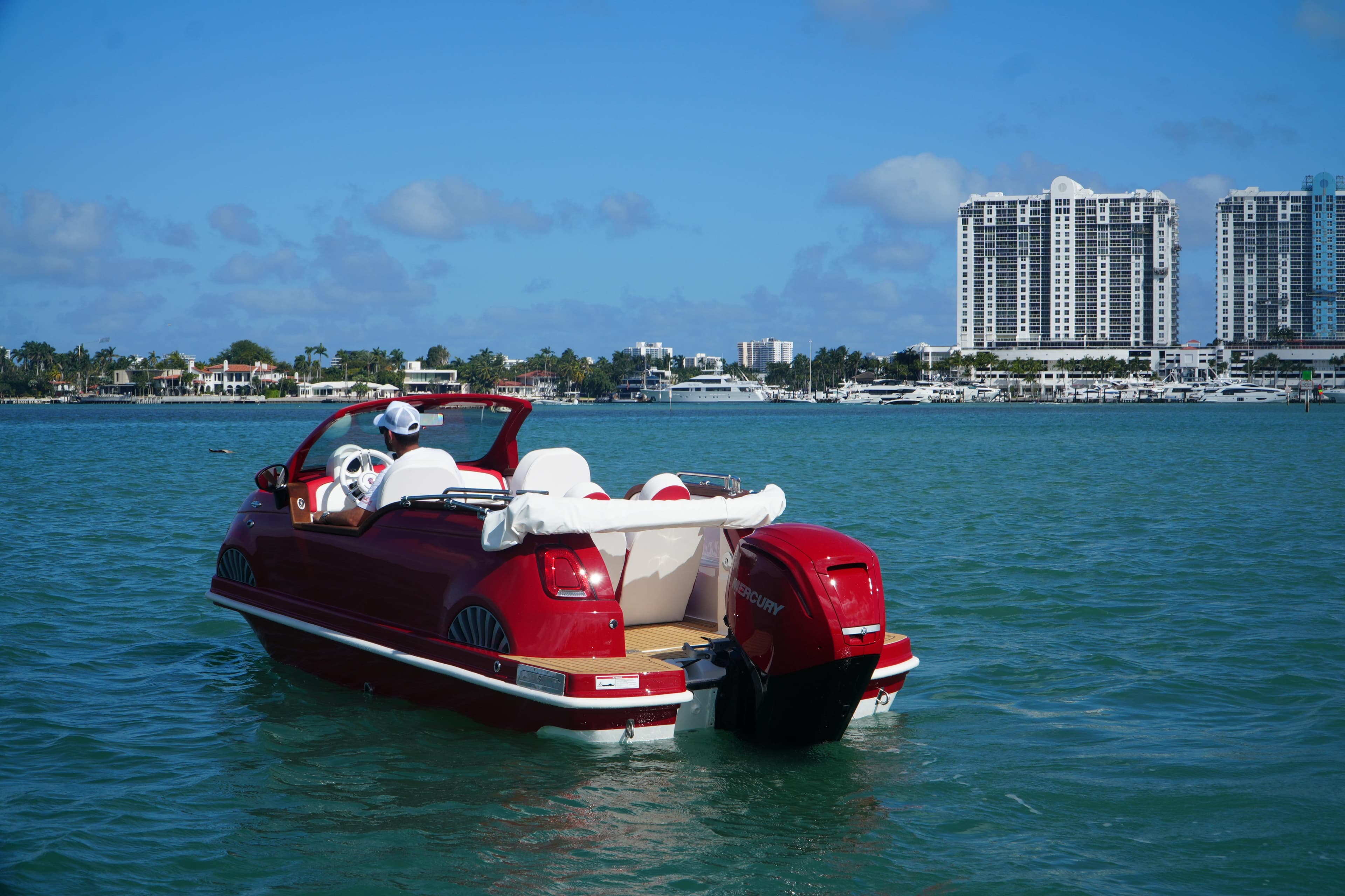 Red Car Off-shore Fiat 500 Classic boat on water, city skyline in background, 2025 model.