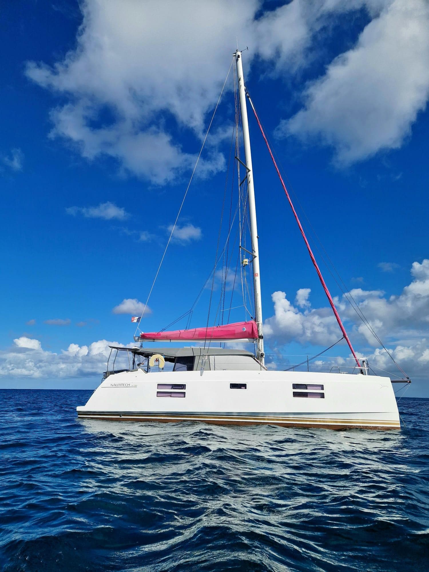 2019 Nautitech 40 Open catamaran sailing on clear blue ocean under a vibrant sky.