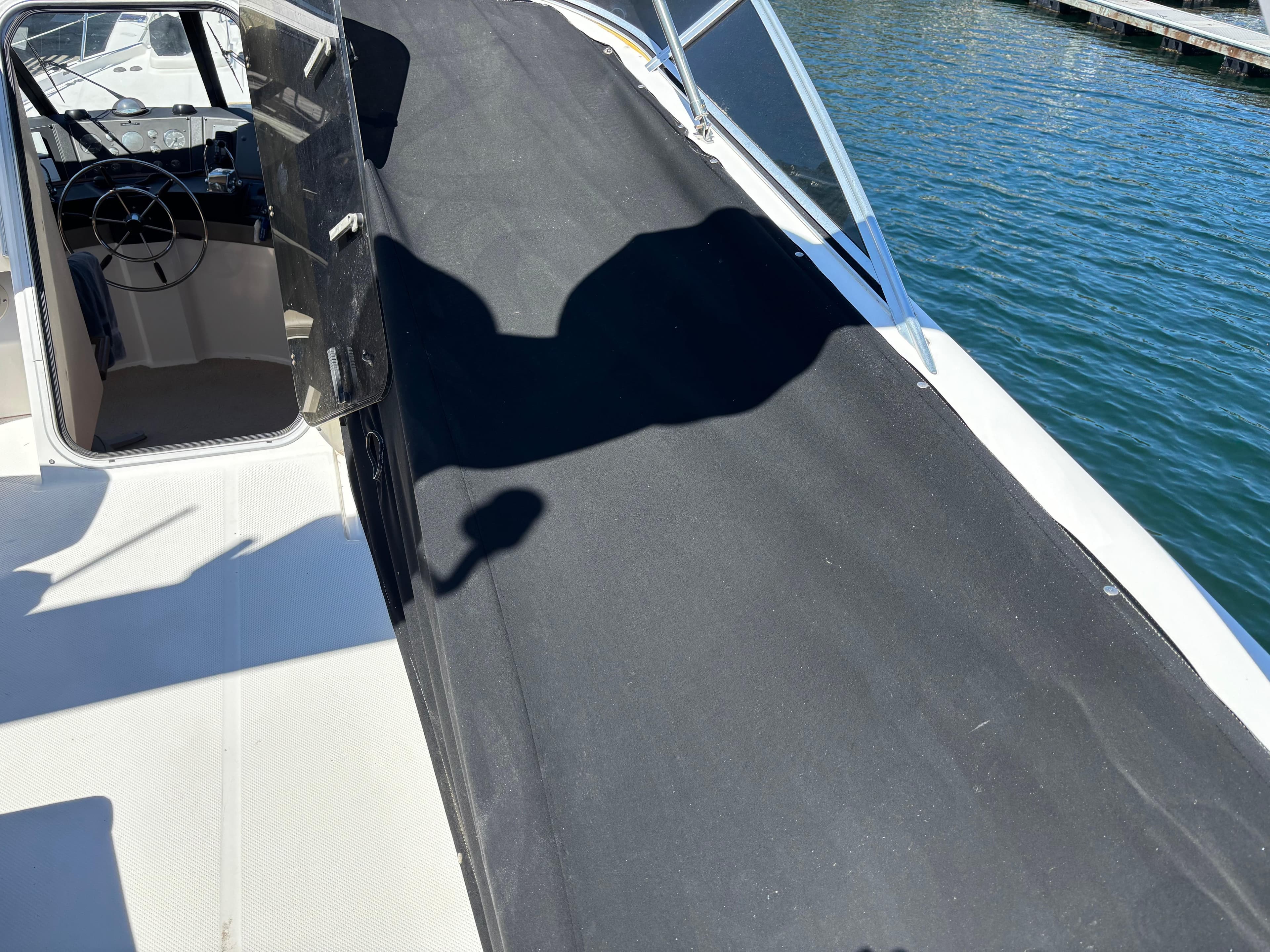 1994 Bayliner 4700 boat deck with black cover, docked by the water.