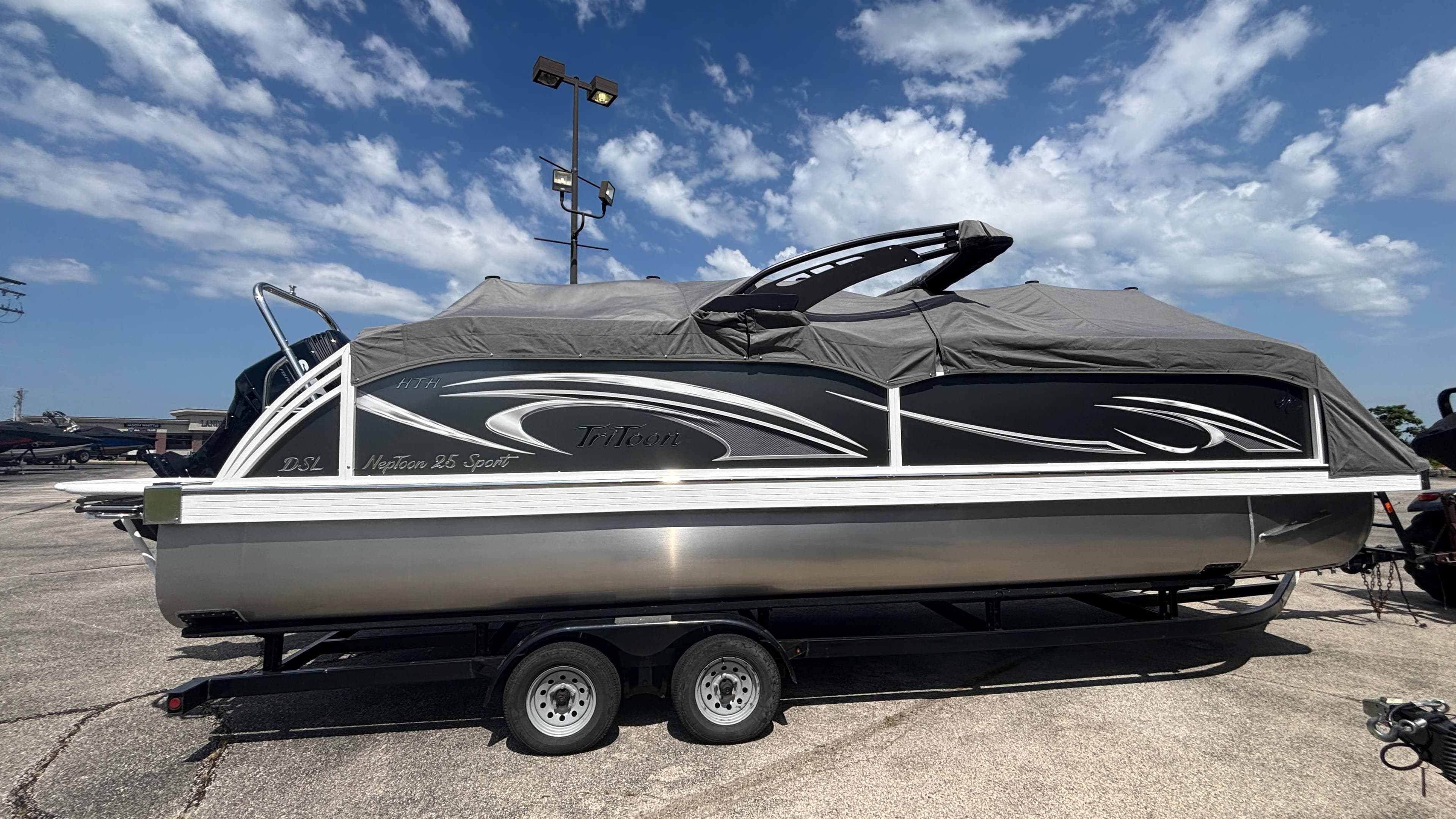 2025 JC Neptoon 25TT Sport pontoon boat on trailer under a cloudy sky.
