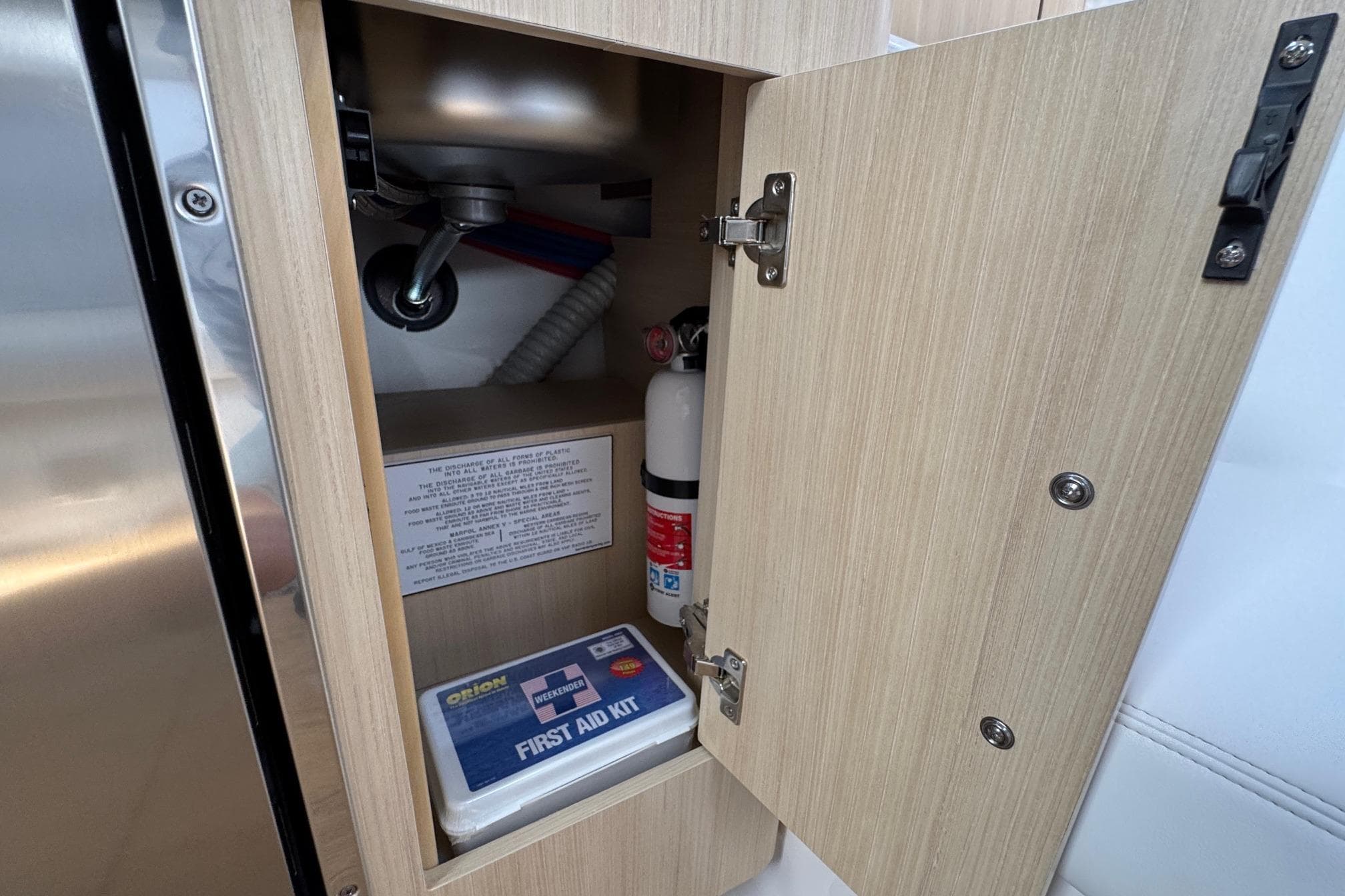 Open cabinet on Regal 33 XO 2026 boat with first aid kit and fire extinguisher.