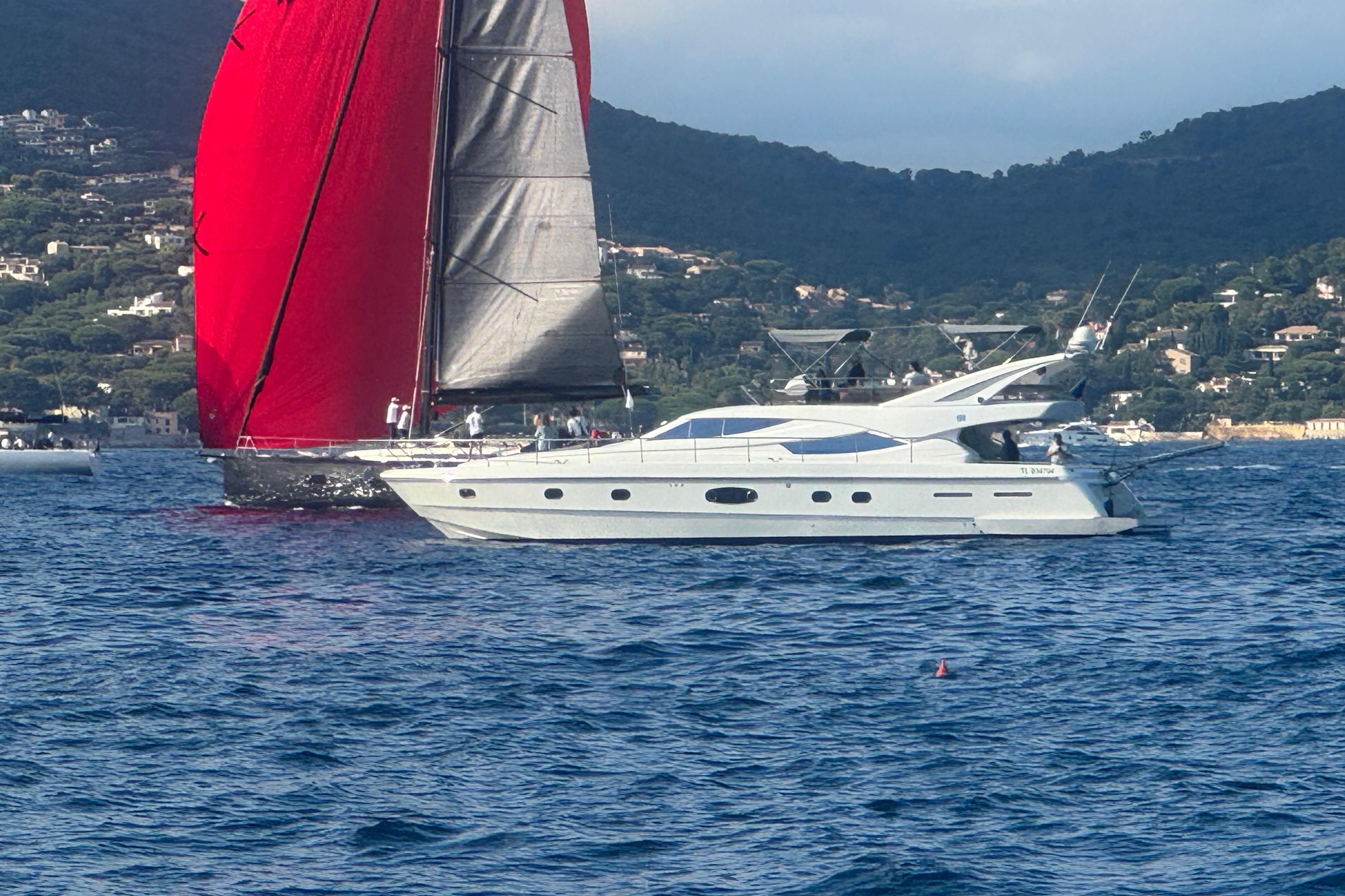 2003 Ferretti Yachts 620 cruising alongside a sailboat with red sails on a scenic coastline.