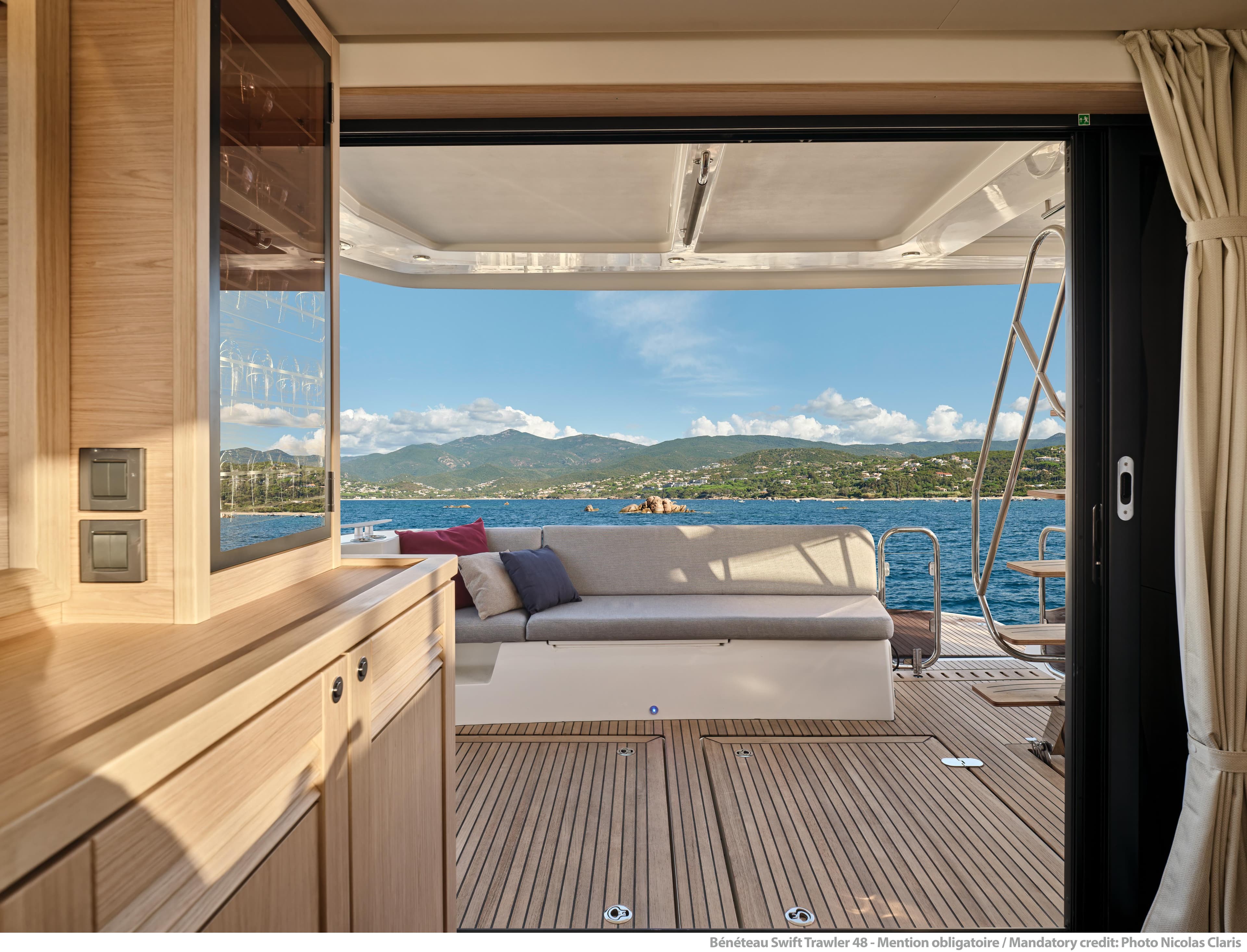 Interior view of 2026 Beneteau Swift Trawler 48, showcasing elegant wood finish and ocean backdrop.