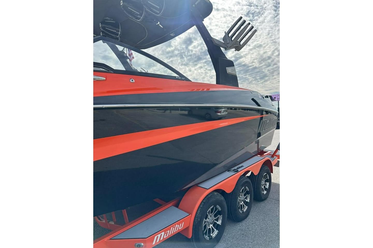 2017 Malibu M235 boat with vibrant orange and black design on a triple-axle trailer.