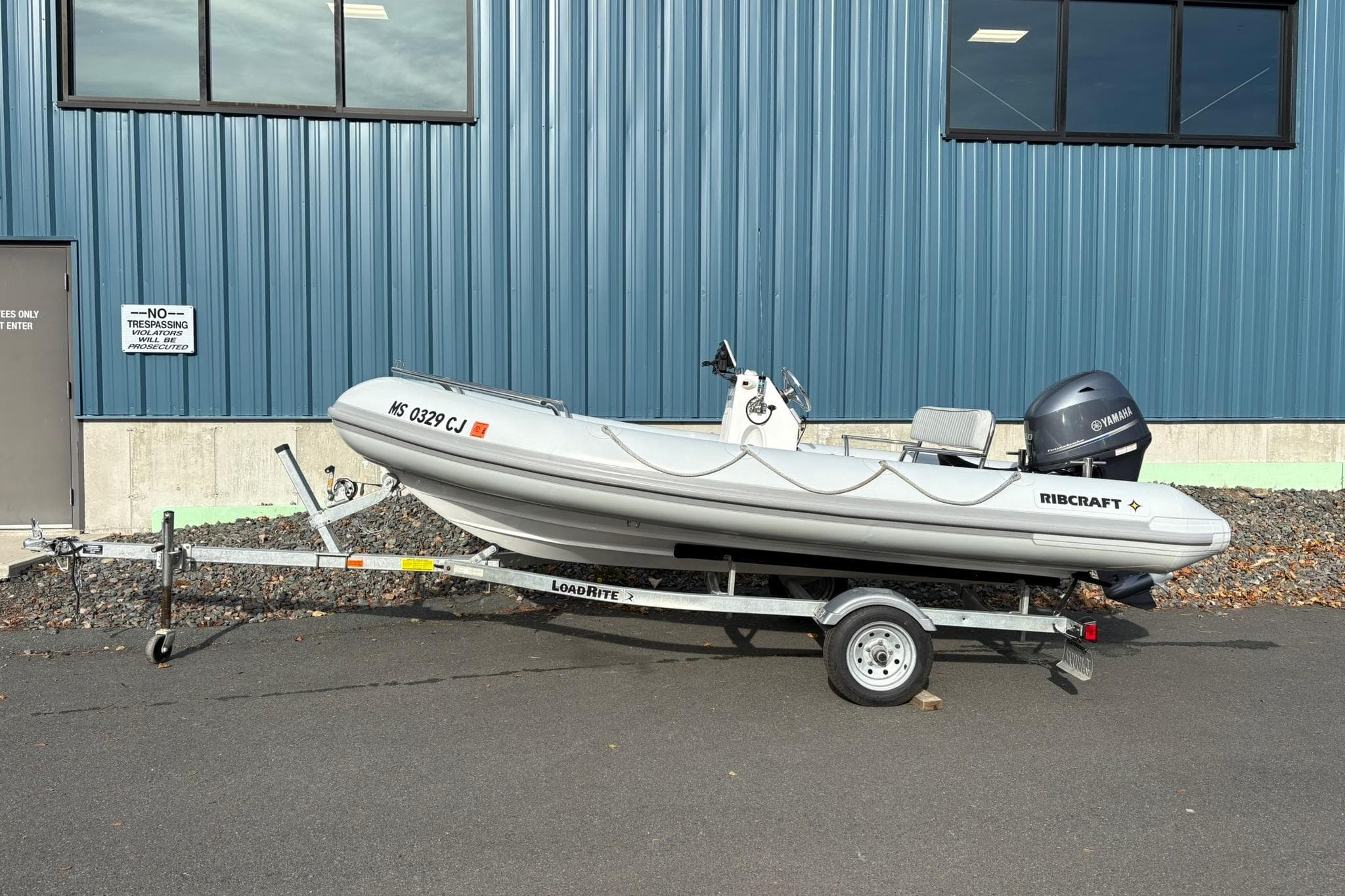 2024 Ribcraft 4.8T inflatable boat on trailer, parked by blue industrial building.