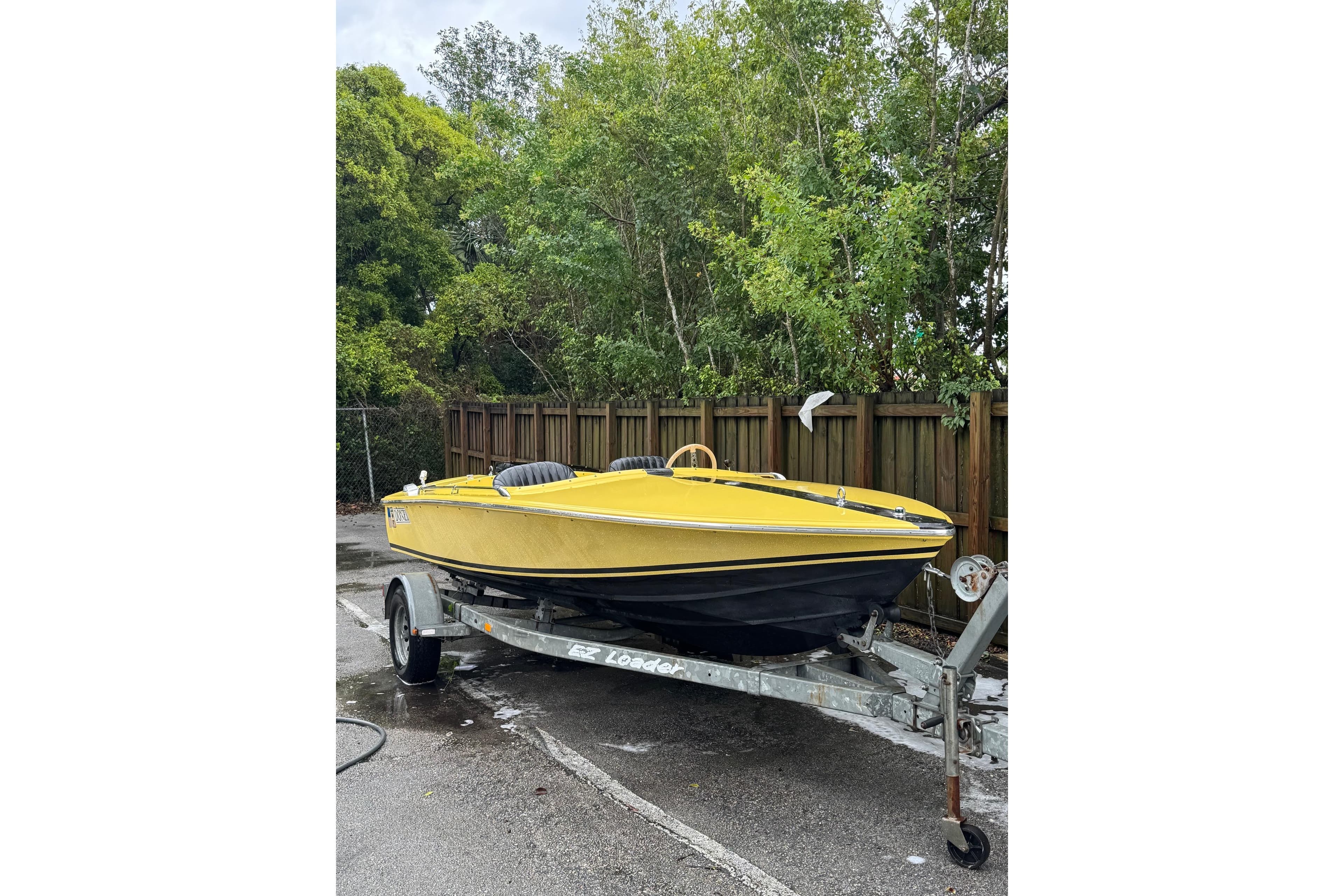 Yellow 1987 Donzi 16 Classic boat on trailer, parked near wooden fence and trees.