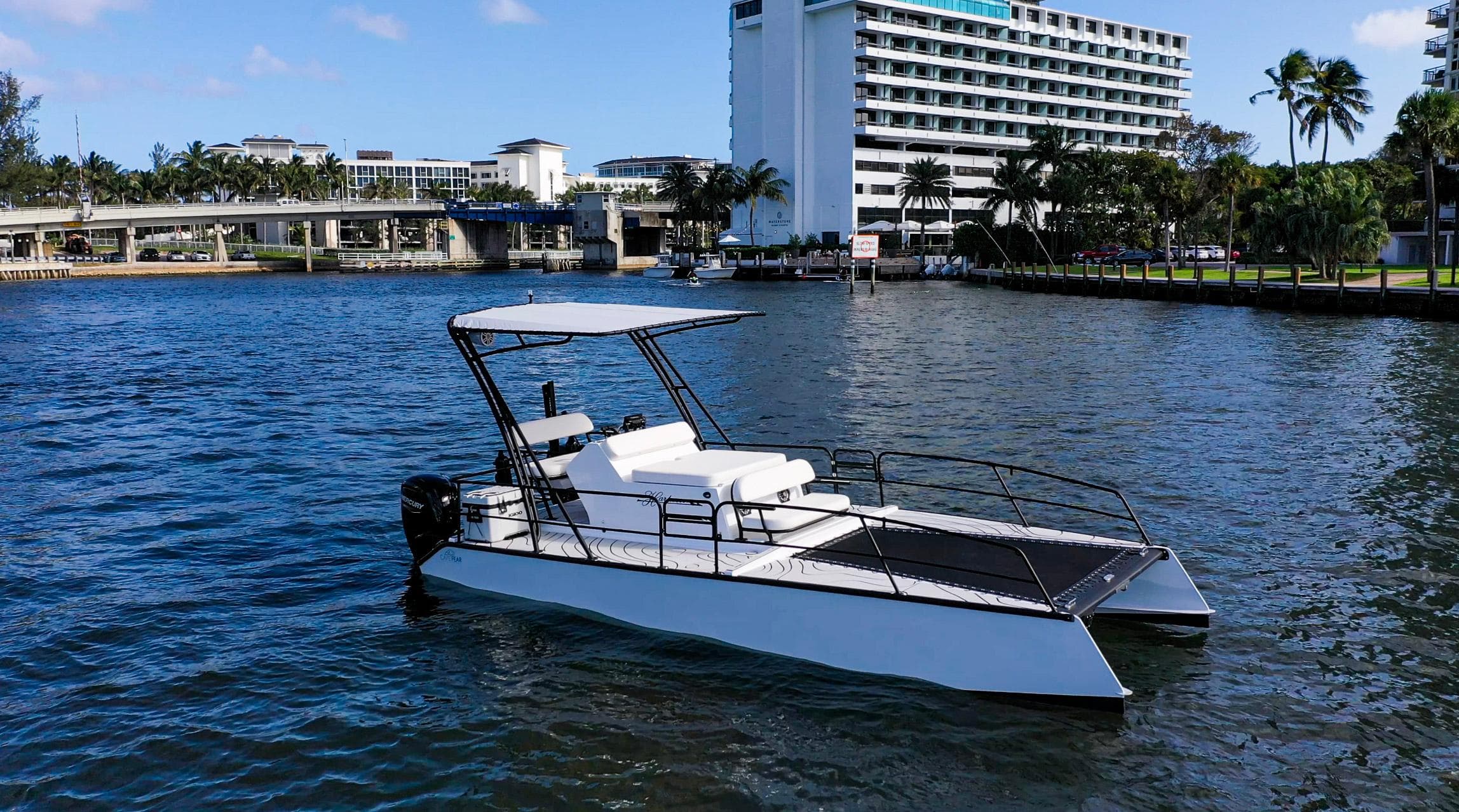 2025 Pontoon Harpoon boat on a scenic waterfront with modern buildings in the background.