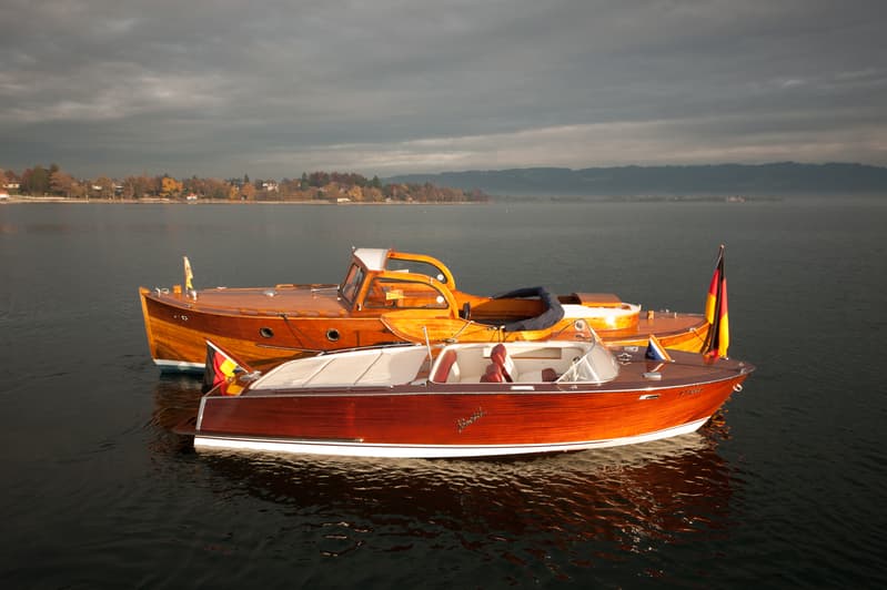 Two classic wooden boats on a calm lake, featuring a 1966 Boesch ACAPULCO 580 deluxe.