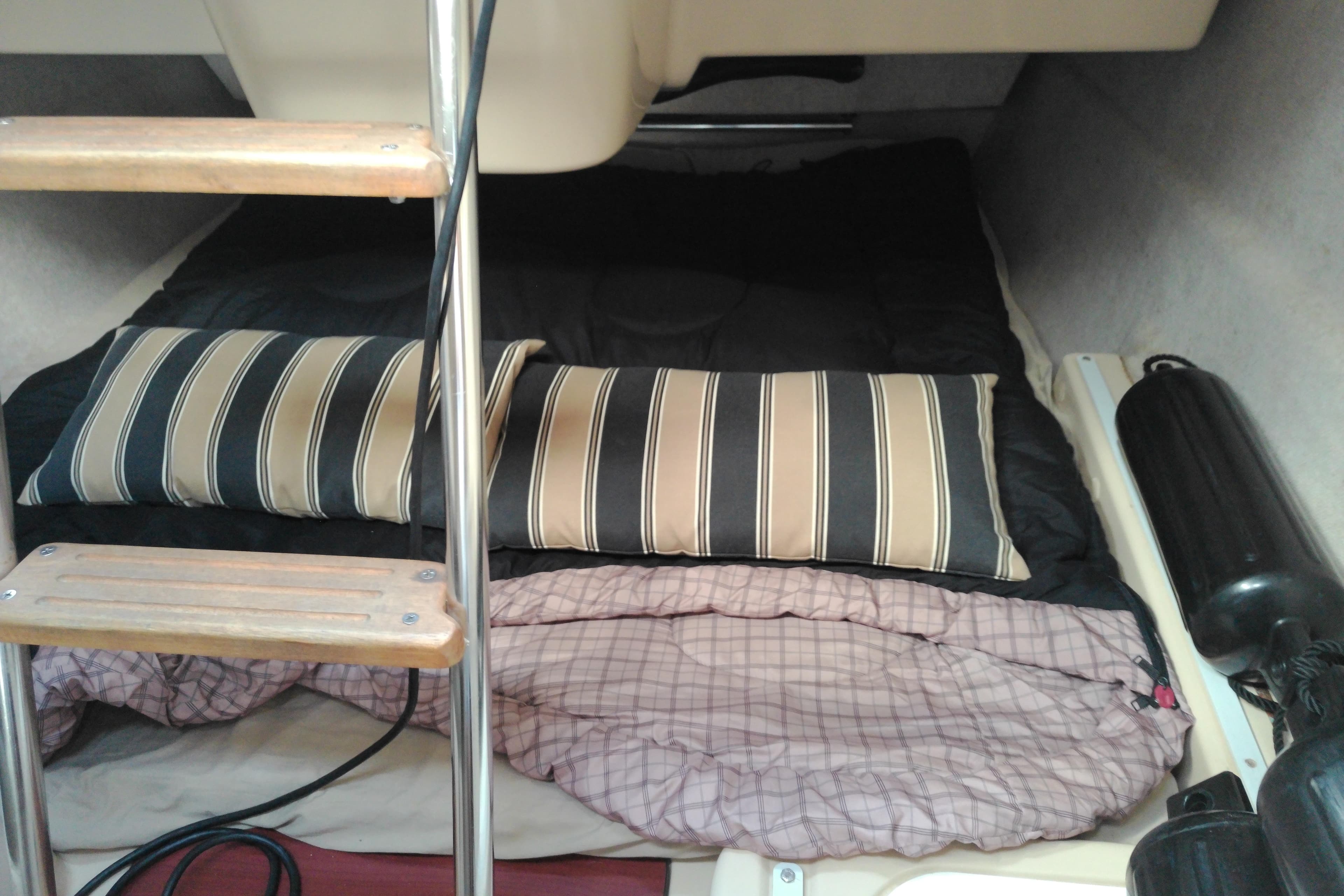Interior cabin of 2011 MacGregor 26M sailboat with striped pillows and sleeping area.